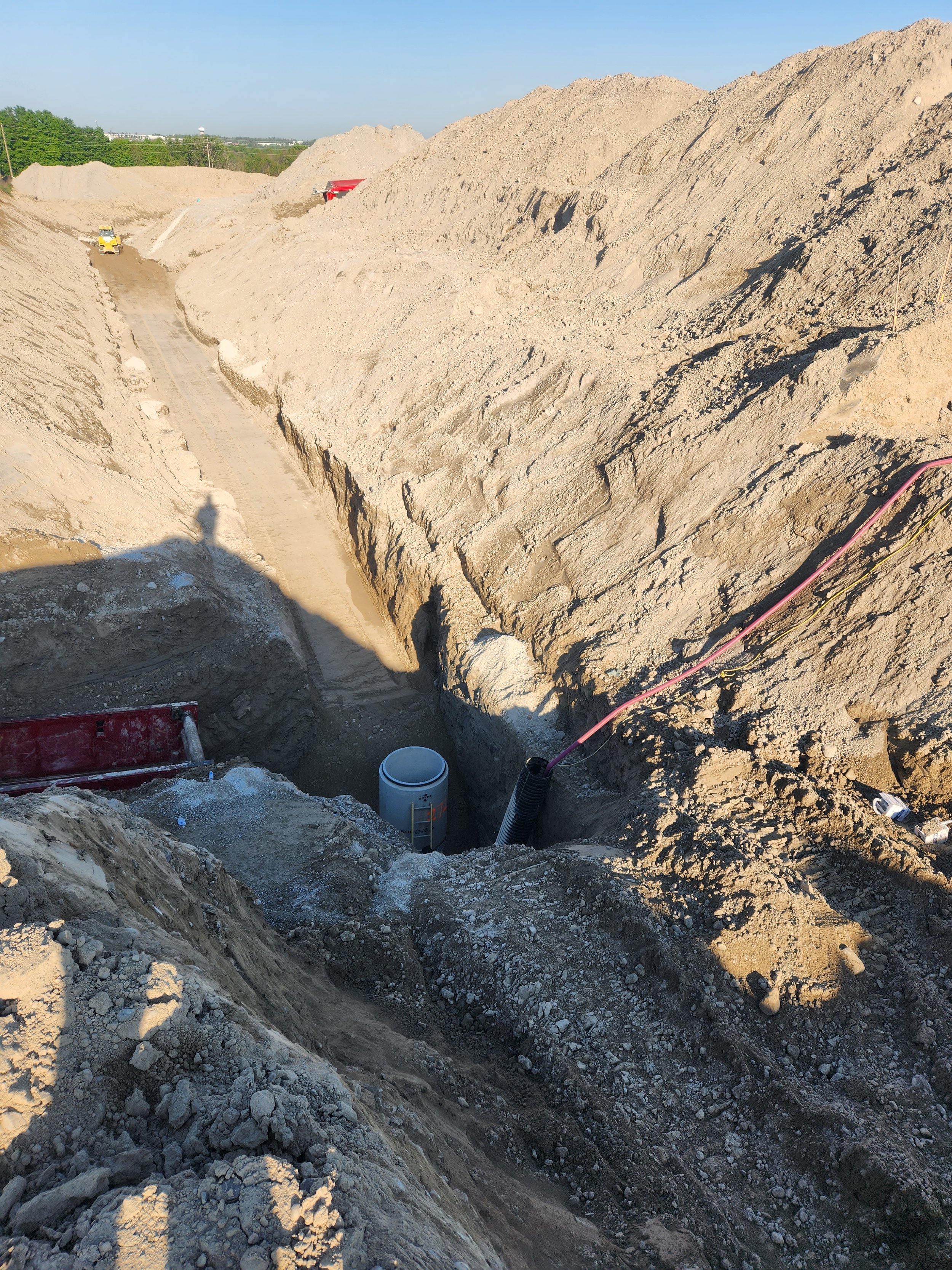 Construction site with dirt excavated to install underground pipes, with construction equipment and a trench.