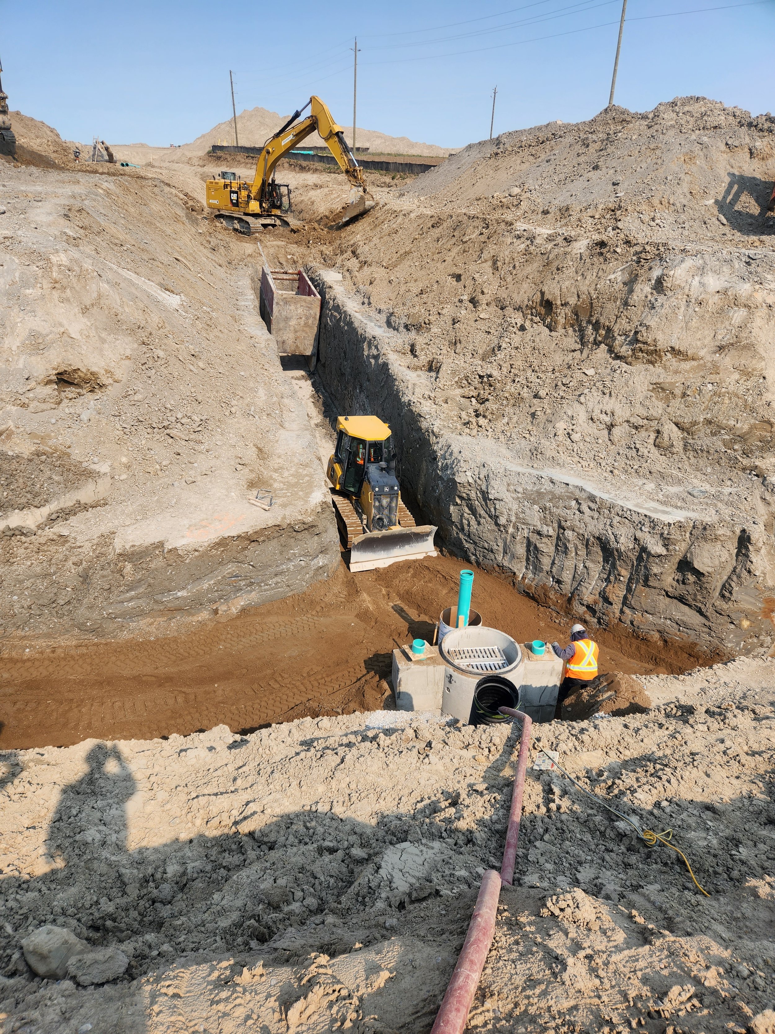 Construction workers and heavy machinery working on a pipeline installation project in a large excavation site.