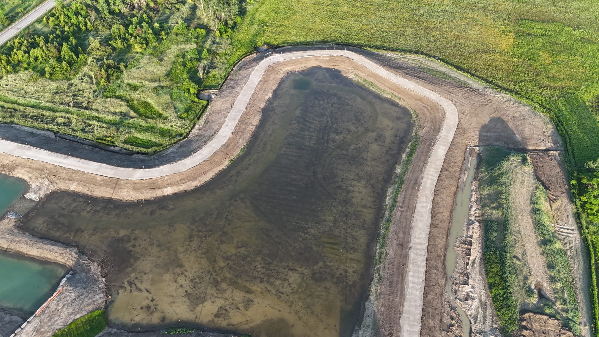Aerial view of a construction site next to a body of water, with roads, dirt, and greenery surrounding the area.