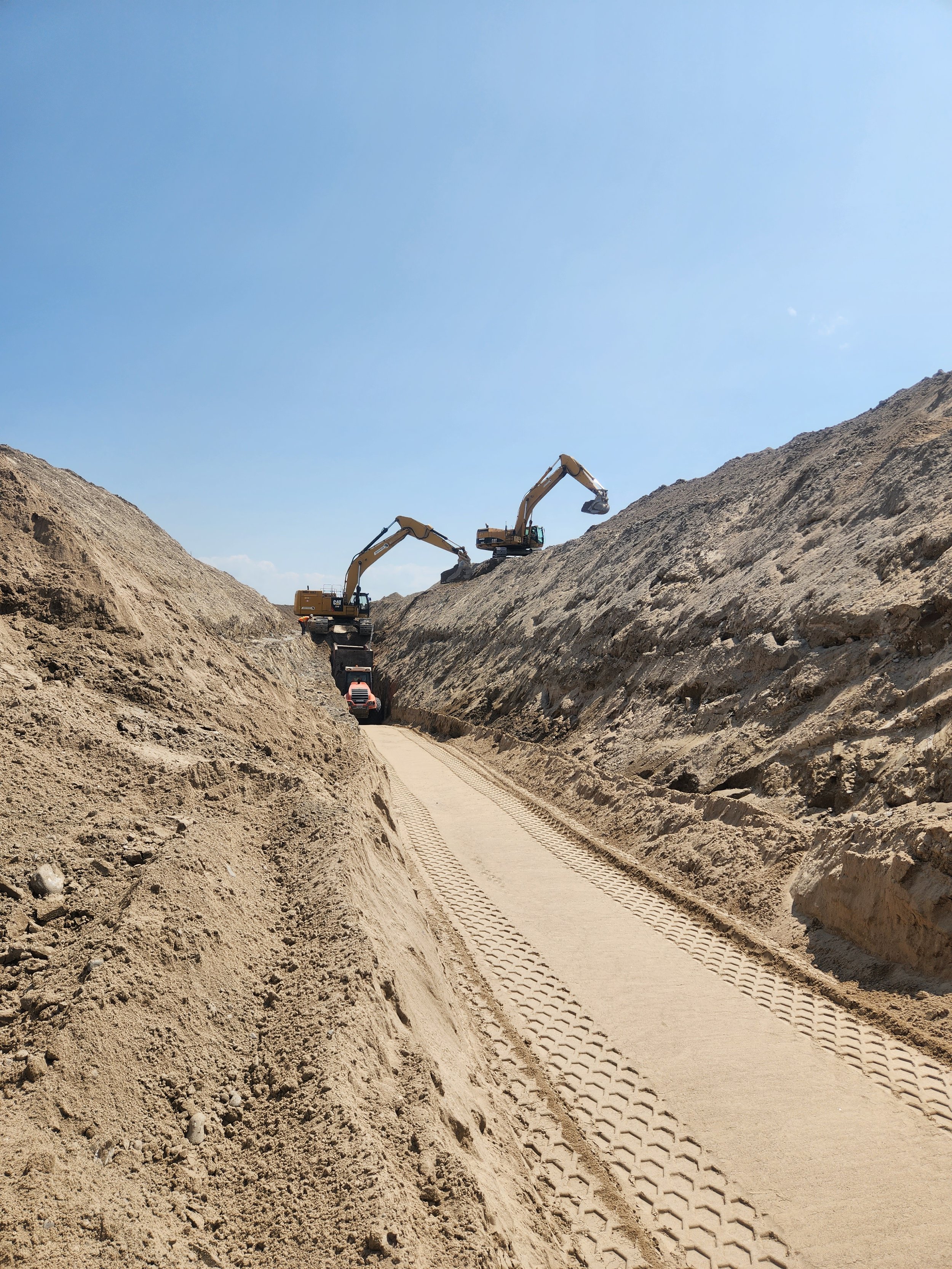 Construction site with excavators on a dirt road under a clear blue sky.