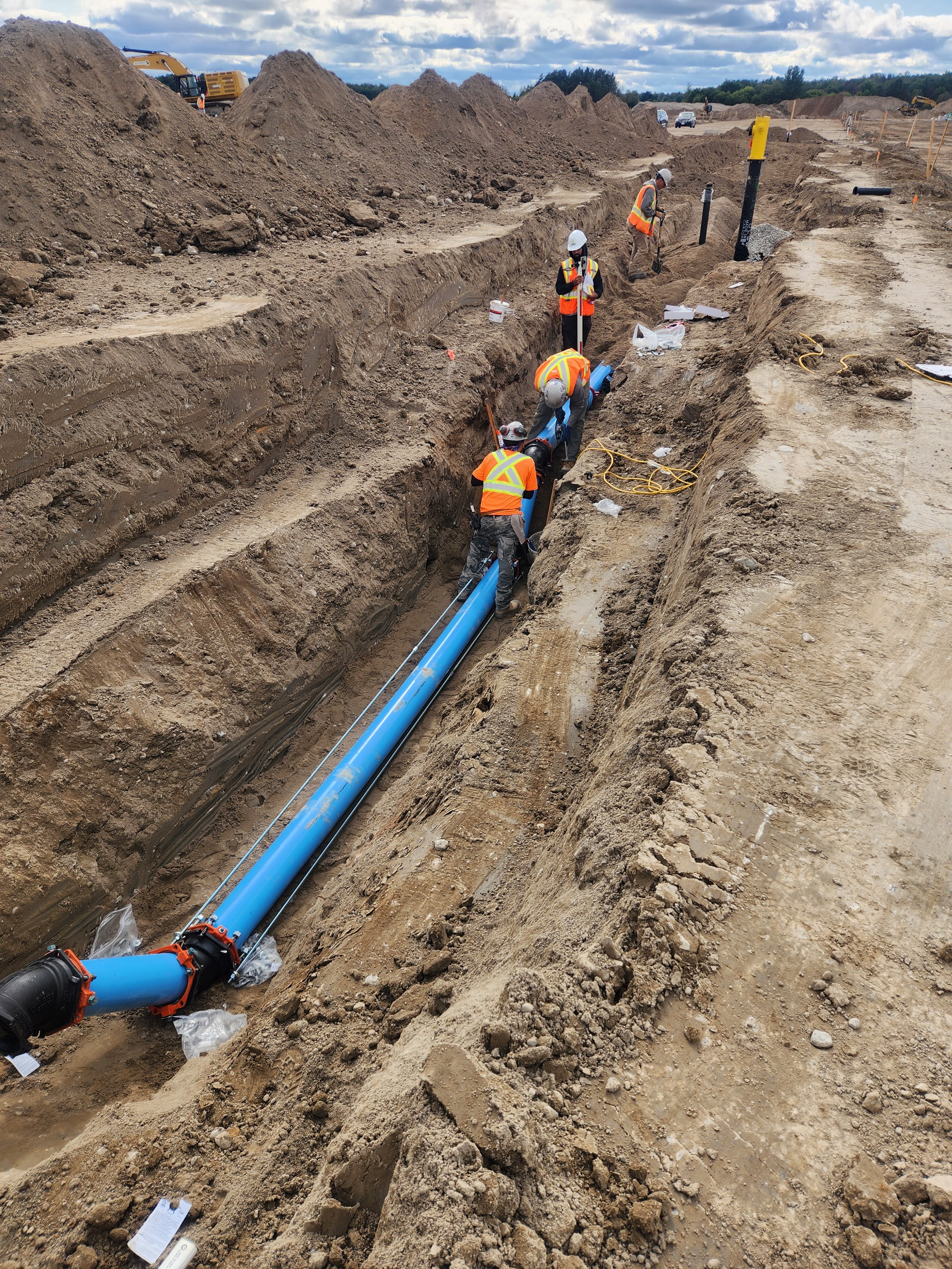 Construction workers installing a large blue pipeline in a deep trench at a construction site.