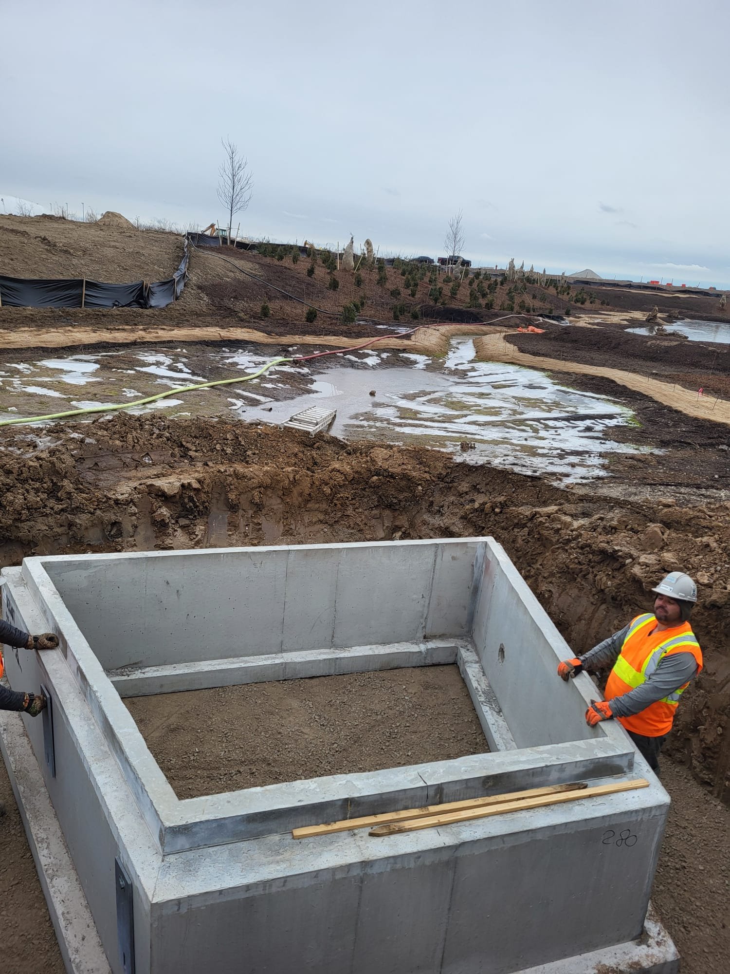 Construction worker in safety vest and helmet standing next to concrete foundation at a construction site.