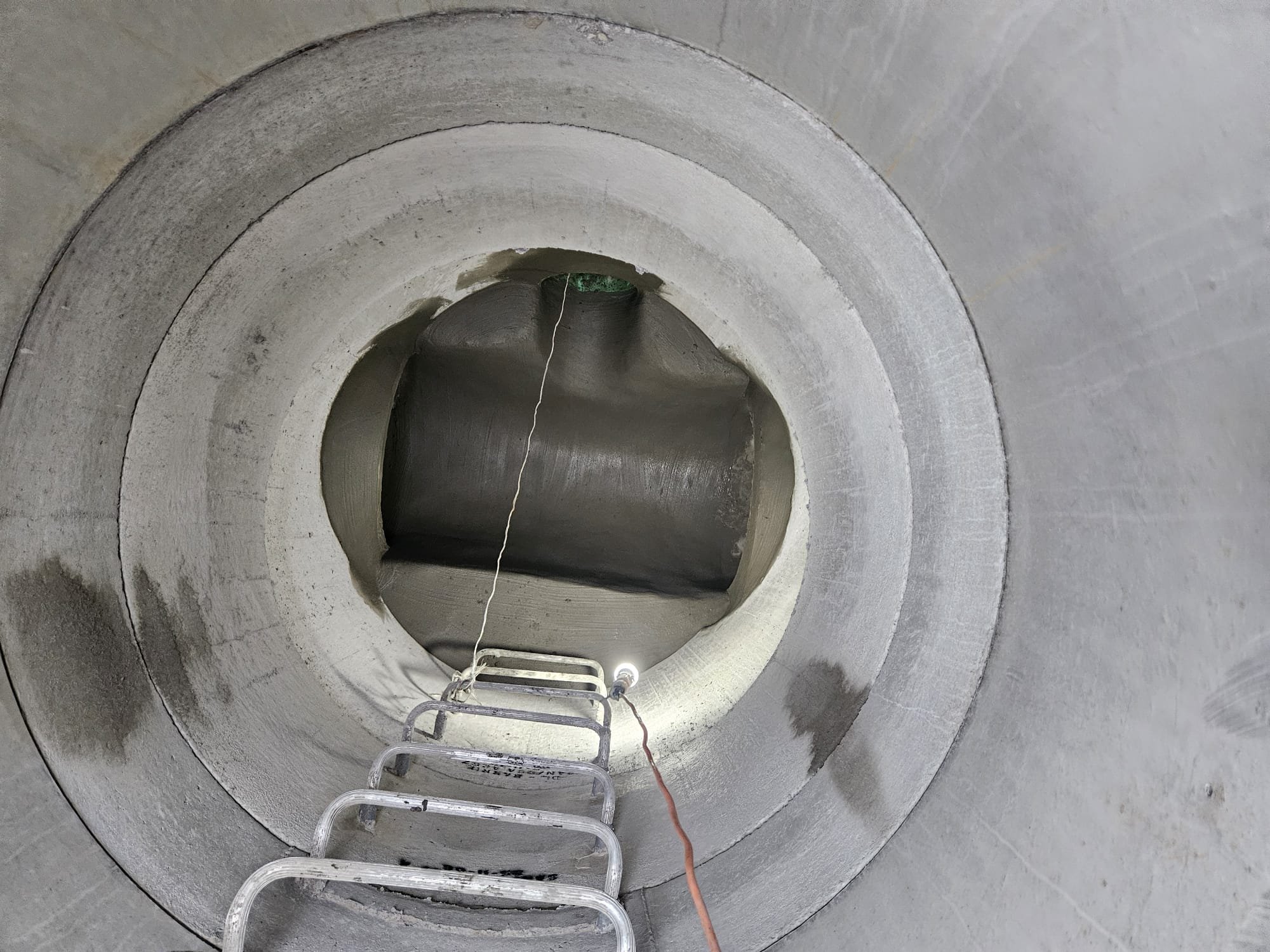 Inside a large concrete pipe with a metal ladder leaning into it, seen from below.