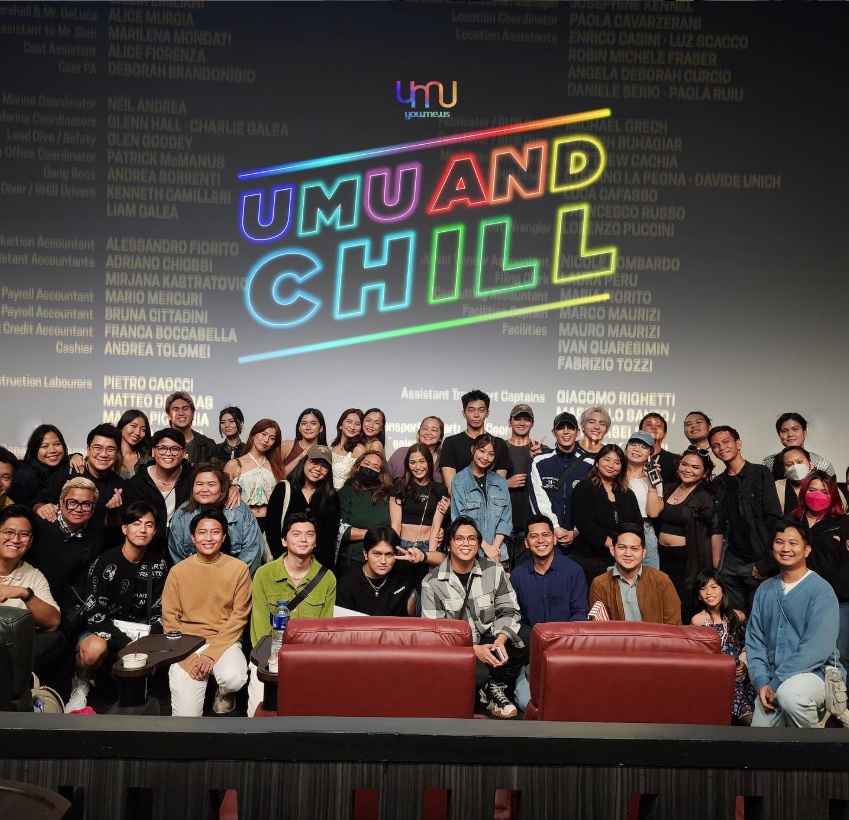 Group photo of diverse young adults and a few children on stage in front of a large projection screen with colorful neon text reading 'UMU AND CHILL' and a list of credits in the background.