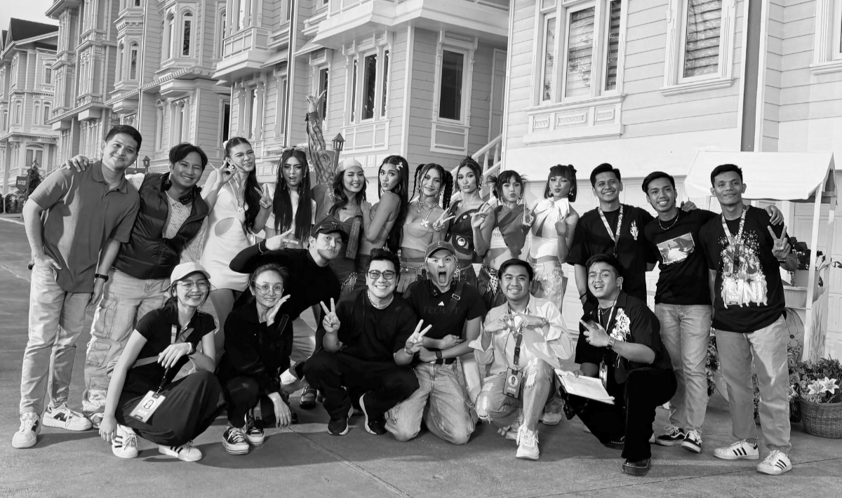 Group of young people smiling and posing for a photo in front of a building, some making peace signs, in black and white.