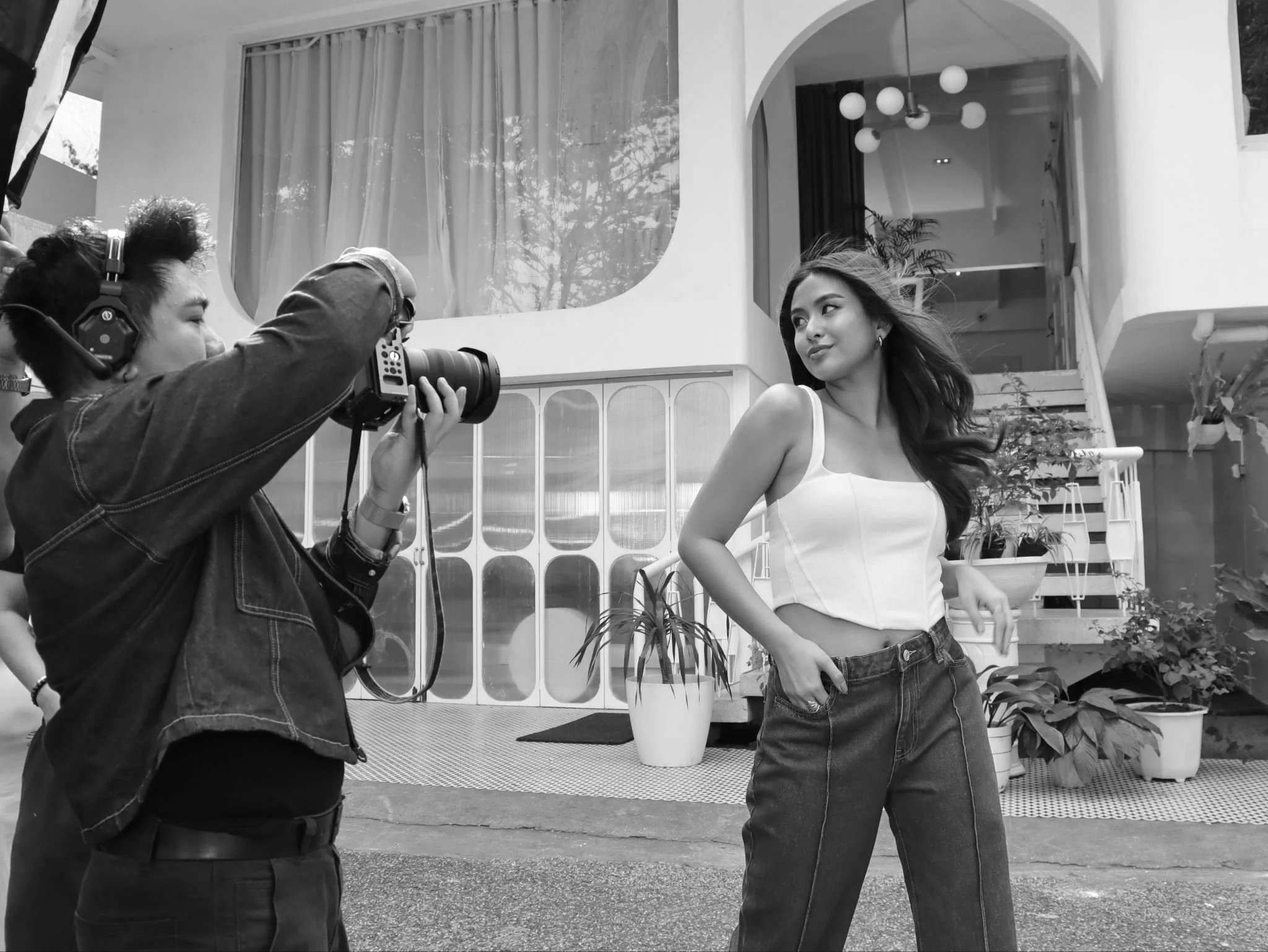 A woman poses for a photograph taken by a photographer outside a modern building with potted plants.