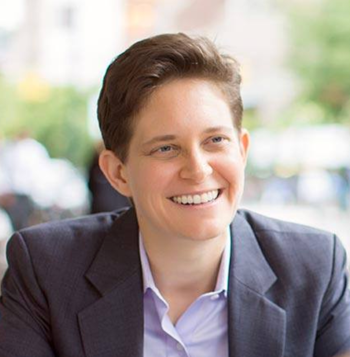 Portrait of a smiling young woman (Dorie Clark) with short brown hair, wearing a blazer and light-colored shirt, sitting in a bright indoor setting.