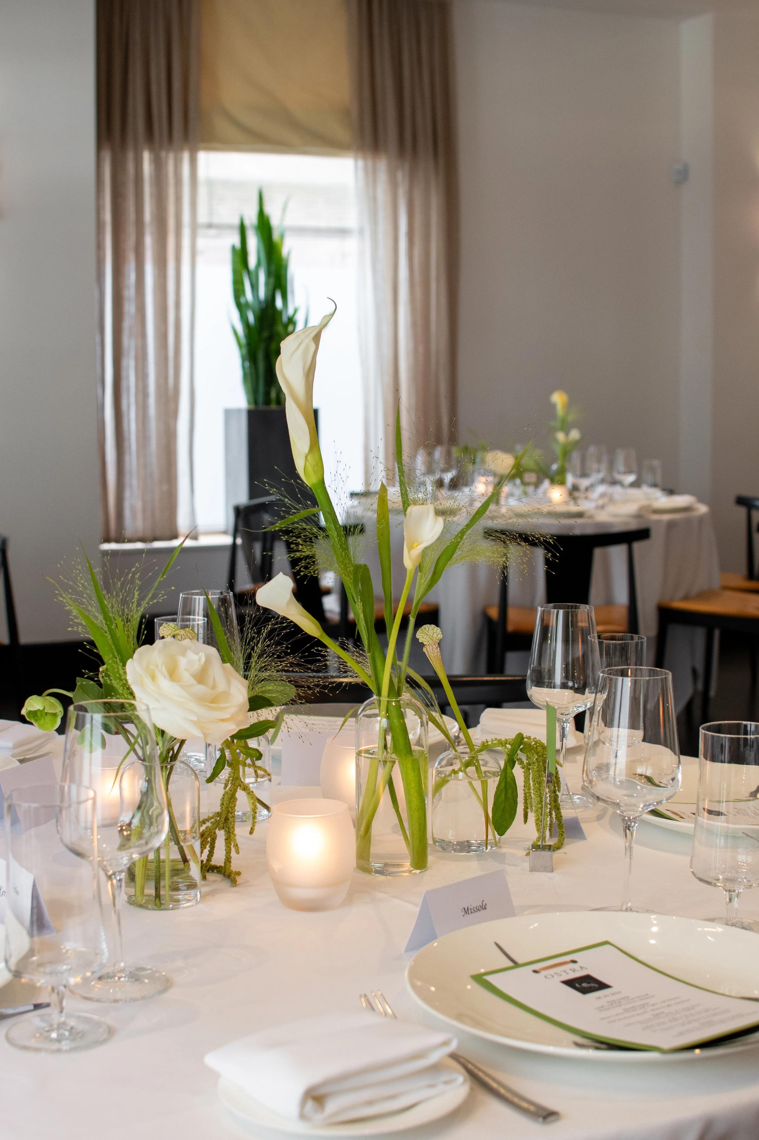 Elegant table setting with white flowers, candles, and glassware in a decorated banquet hall.