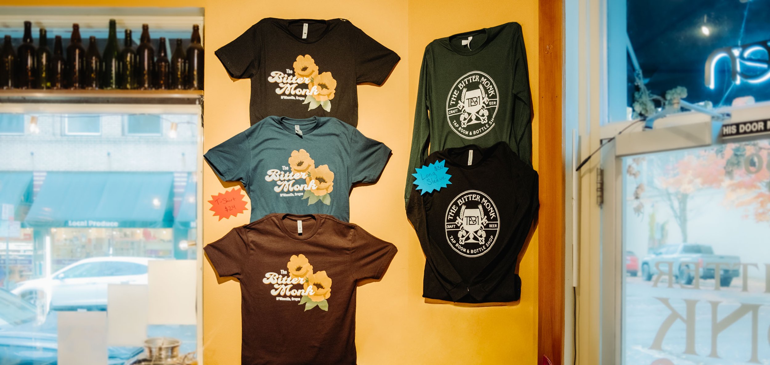 Display of colorful T-shirts with 'The Bitter Monk' logo, merch available for purchase at the craft beer bar on Third Street in McMinnville, Oregon.