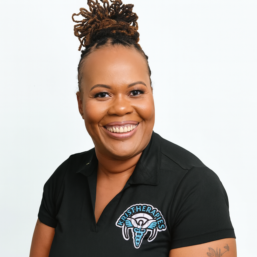 A smiling woman with braided hair styled in dreadlocks tied up, wearing a black polo shirt with a logo that reads 'Krist Therapies' and features a caduceus symbol with wings.