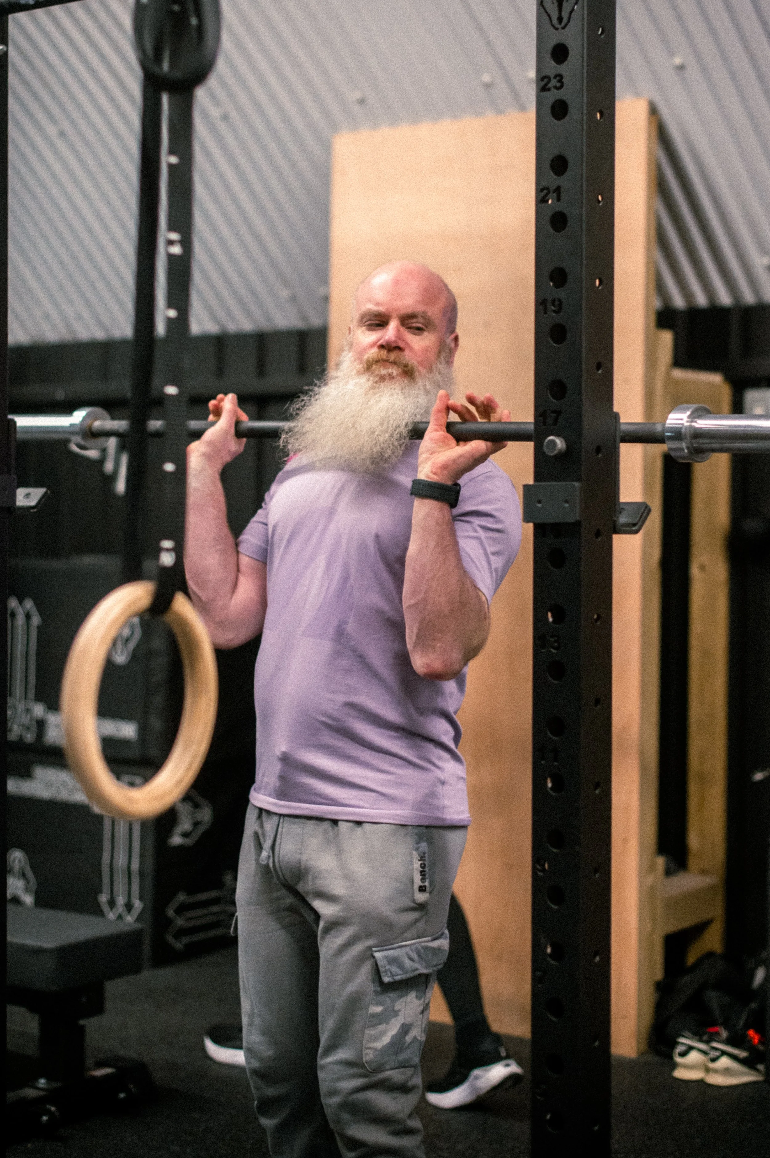 Man with a long white beard lifting a barbell in a gym.