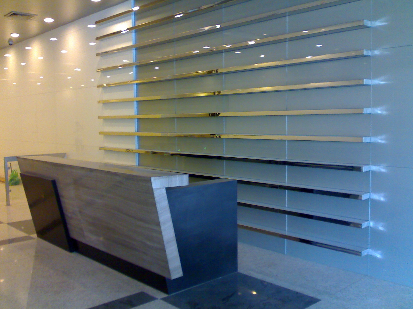 Empty retail store or mall with a glass and metallic wall display and an angled wooden counter.