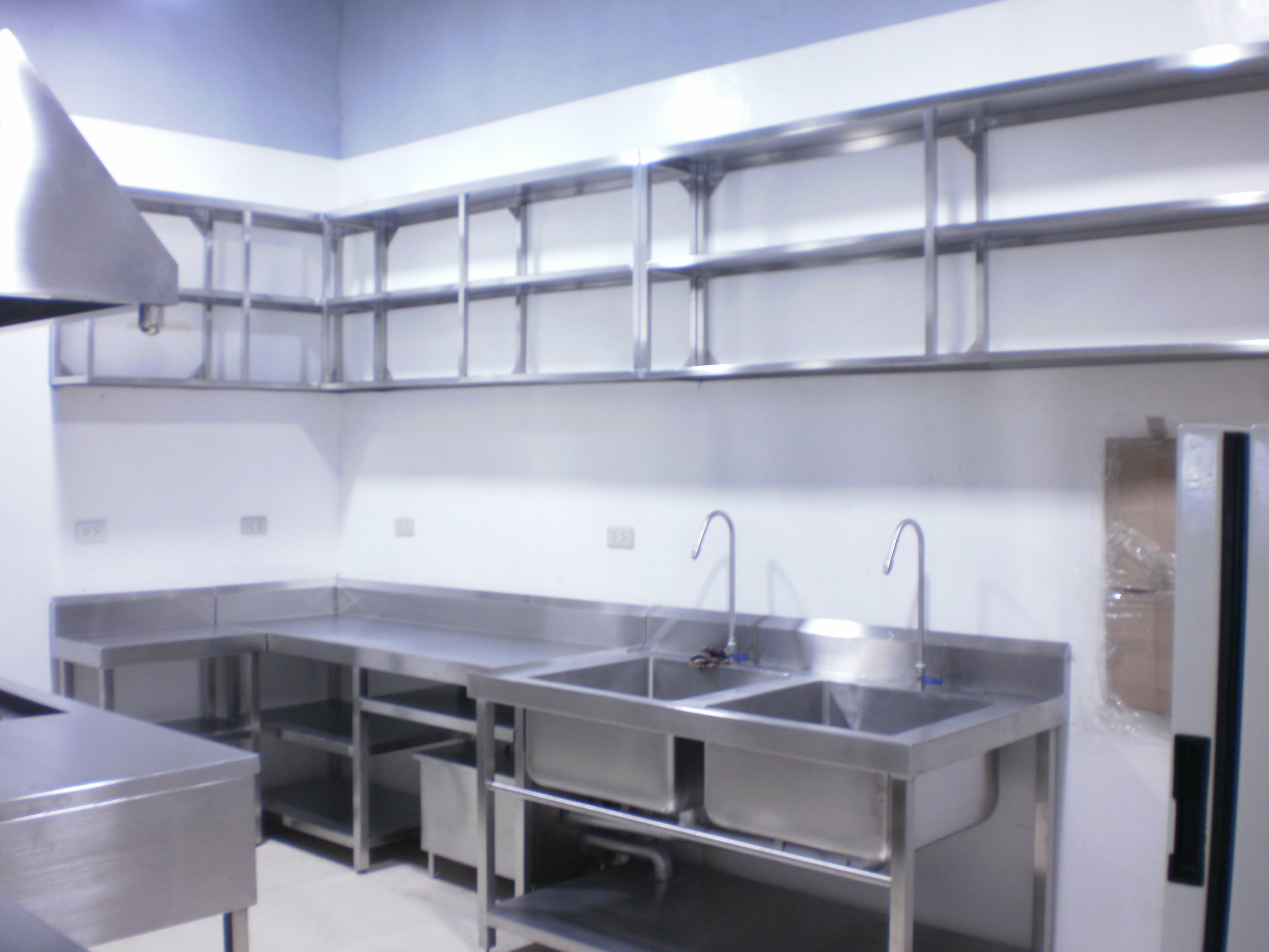 Stainless steel kitchen with two sinks, a countertop, and an upper shelf.