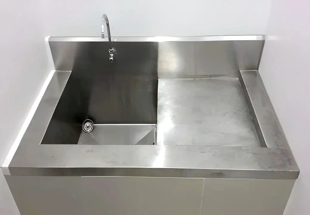 A stainless steel utility sink with a faucet and drain, situated against a white wall.