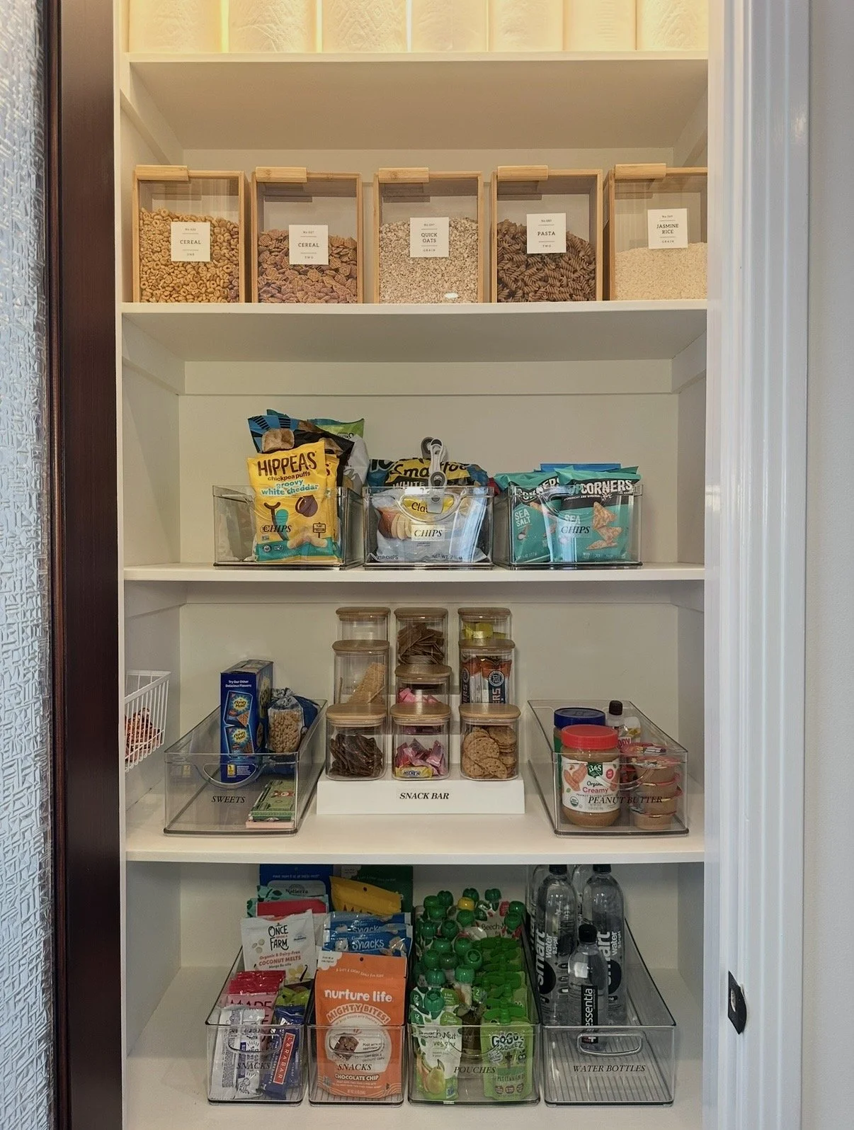 Open pantry with snacks, cereals, water bottles, and other food items organized on shelves.