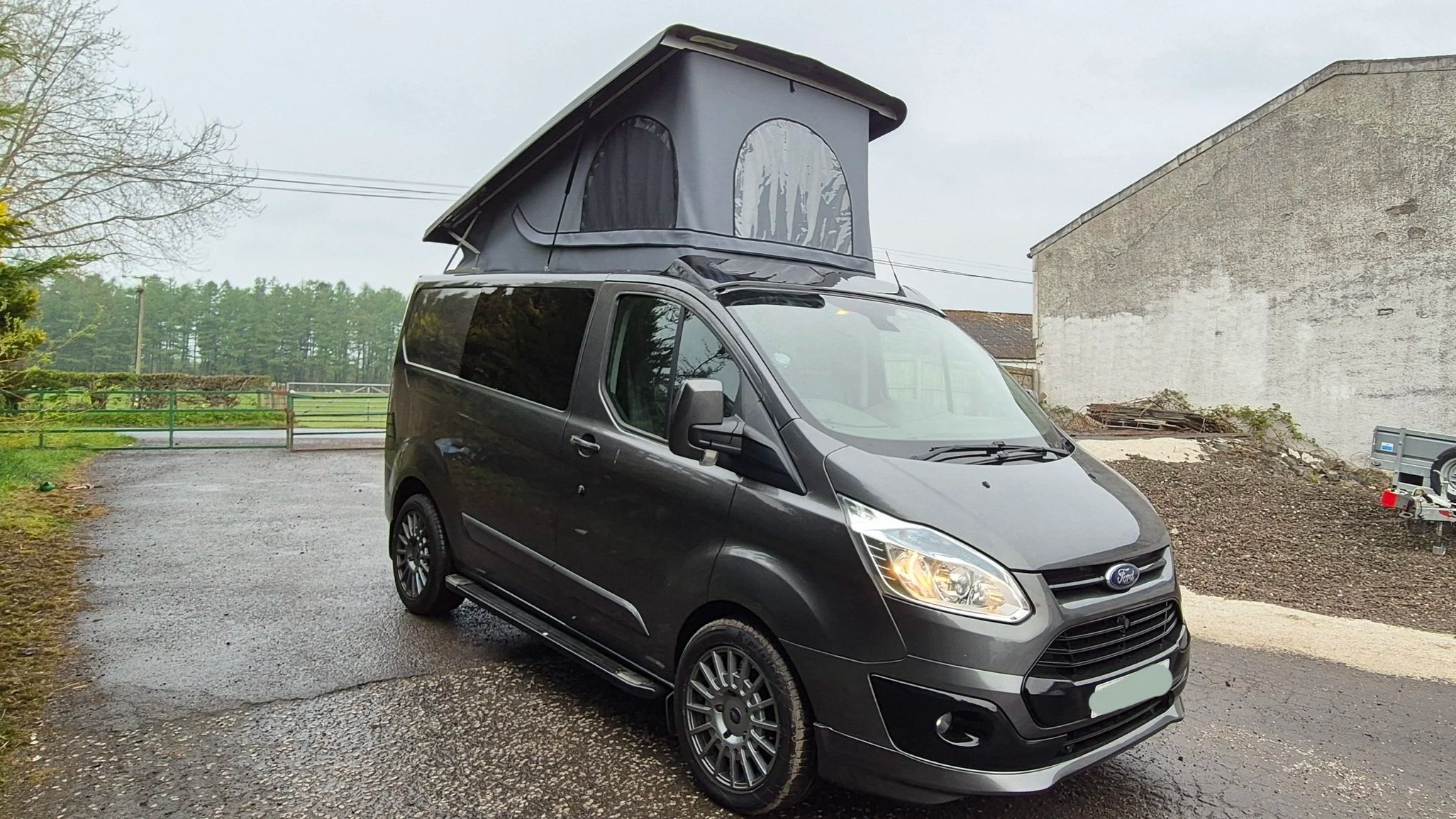 Black campervan with a pop-up roof tent parked on a gravel driveway.