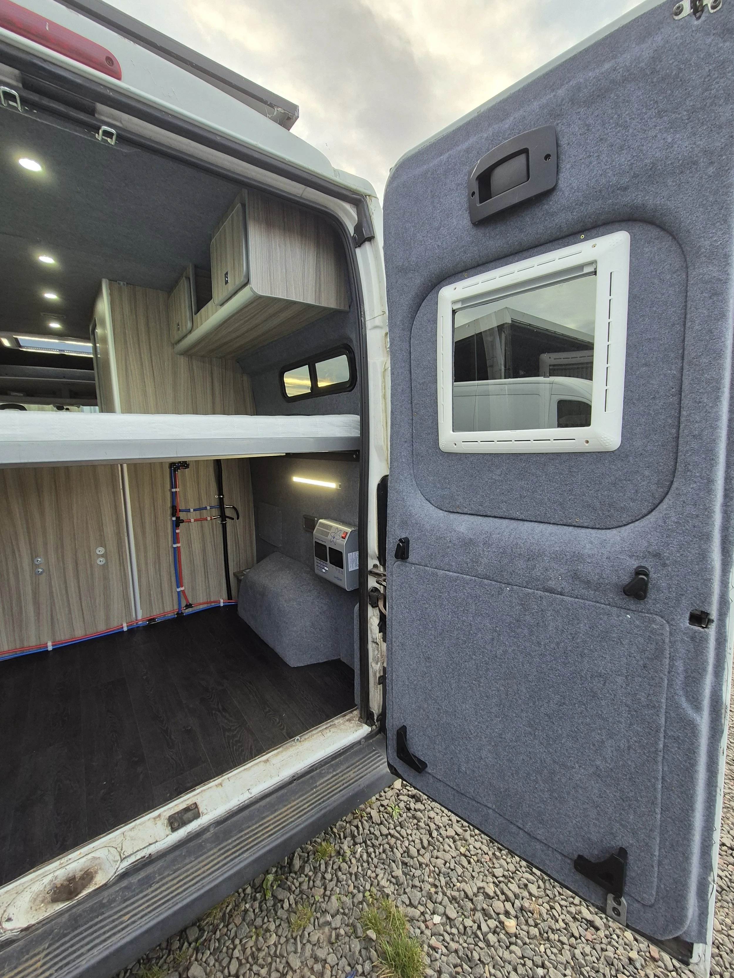 Open door of a converted camper van with interior wood paneling and built-in storage compartments.