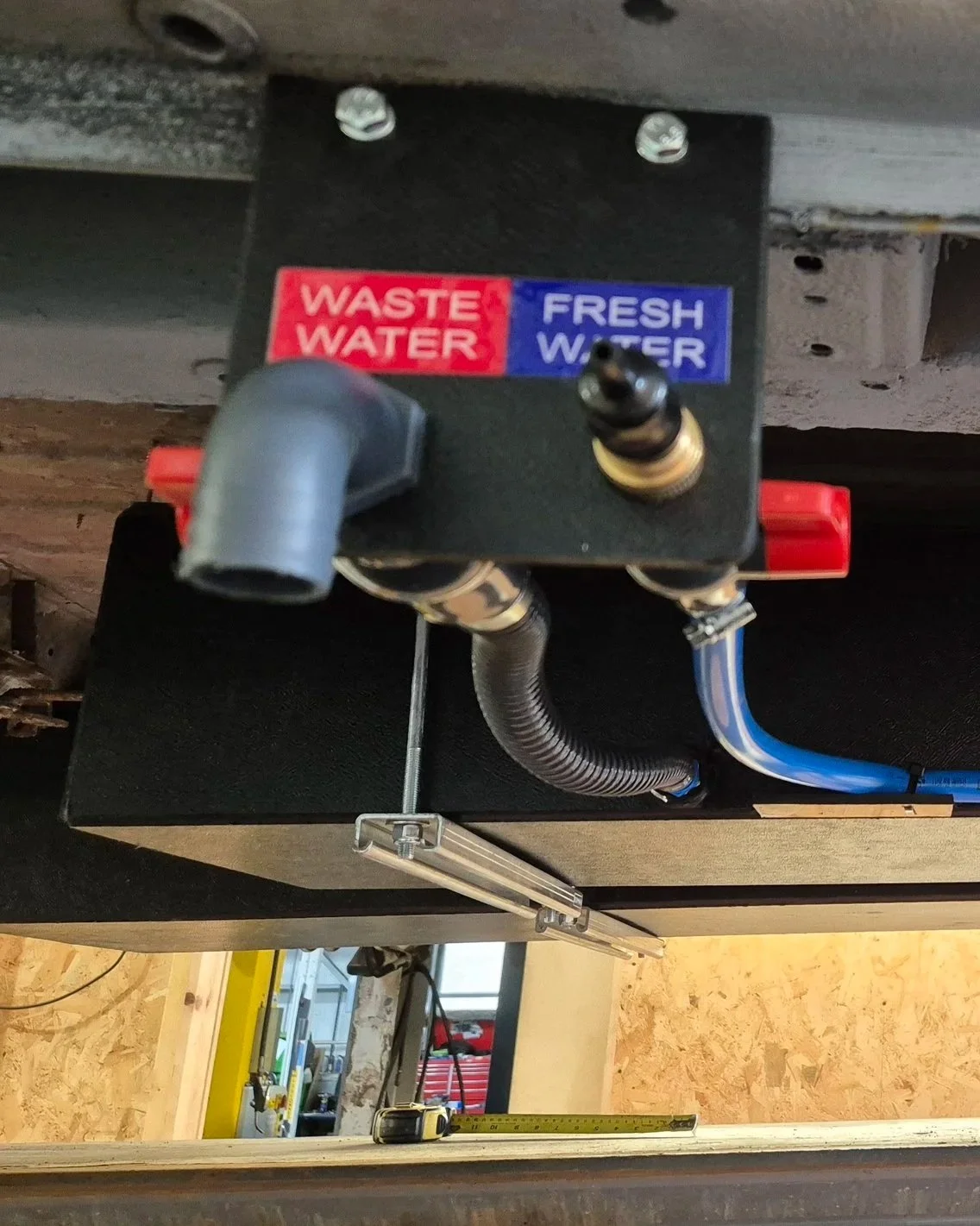A plumbing manifold with labeled outlets for waste water and fresh water, with pipes connected to each labeled outlet.