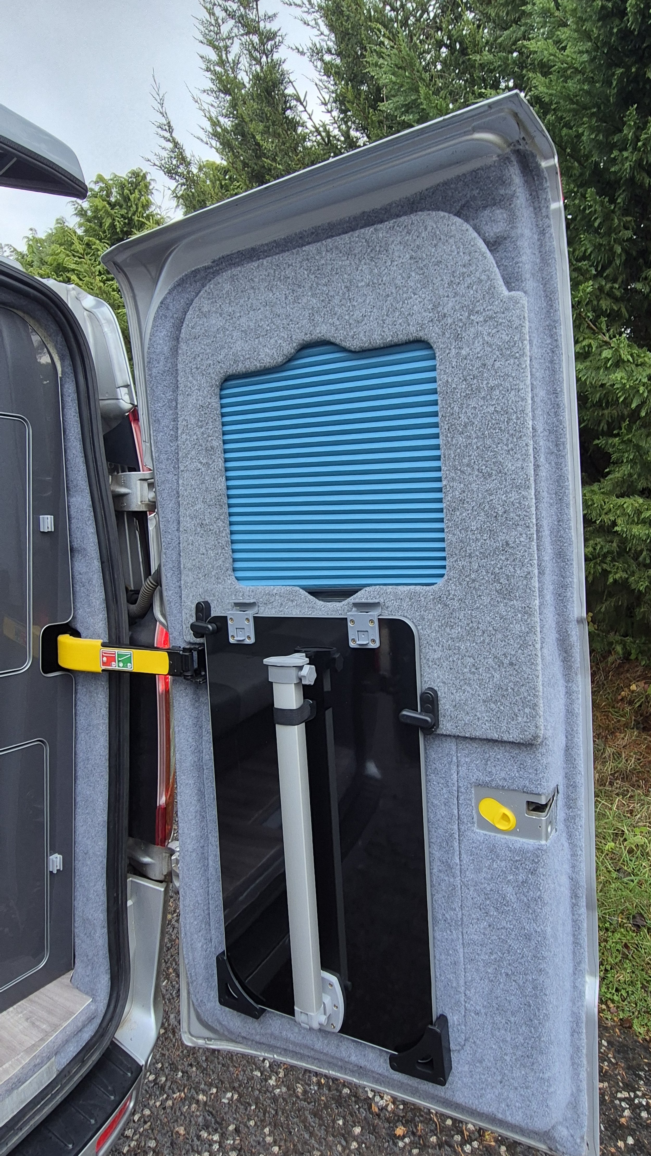 Open vehicle door revealing folding wheelchair lift inside with fabric-lined walls and a blue accordion-style cover.