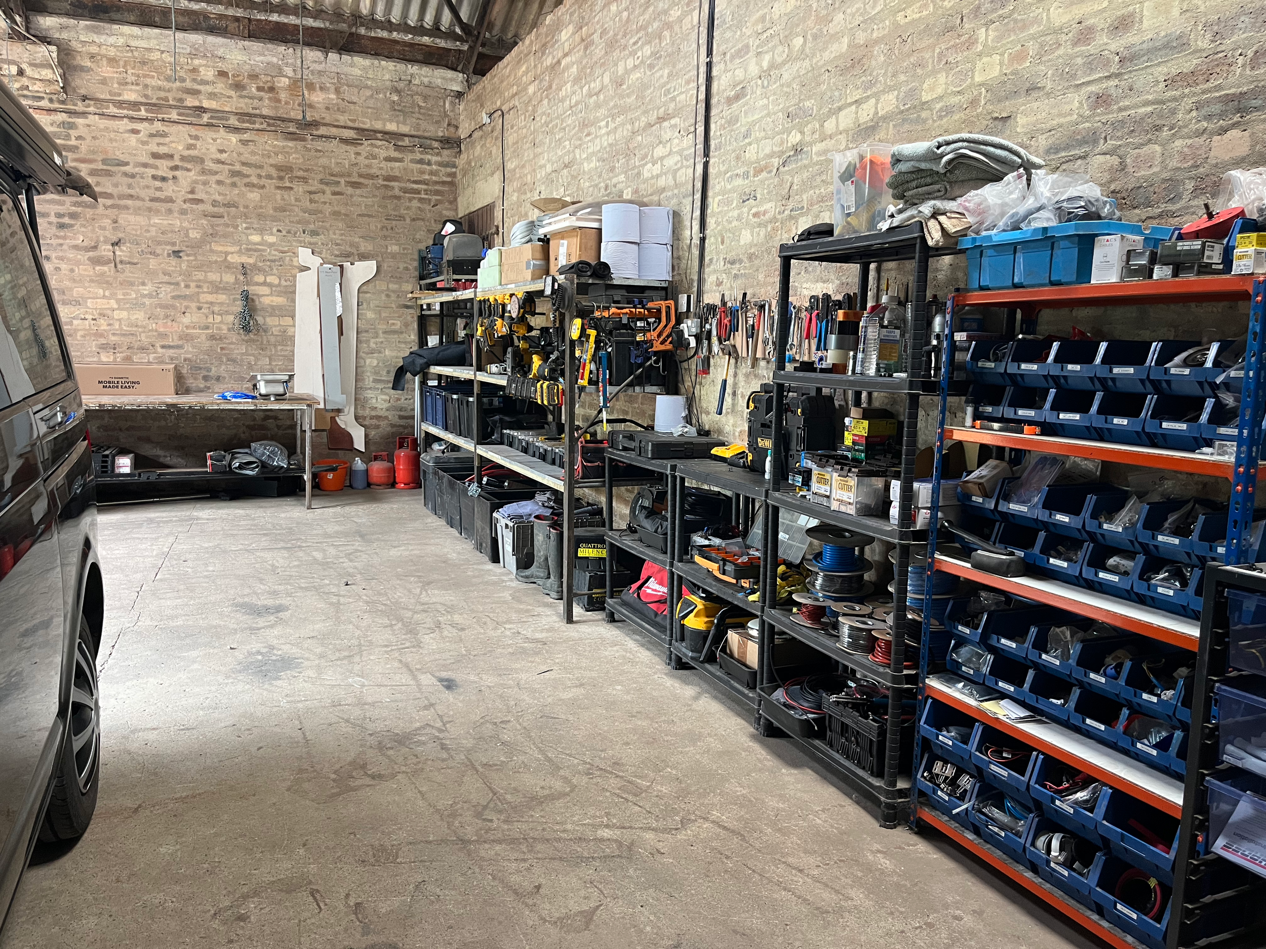 Organized garage with tools and storage shelves along a brick wall, partially visible vehicle on the left.