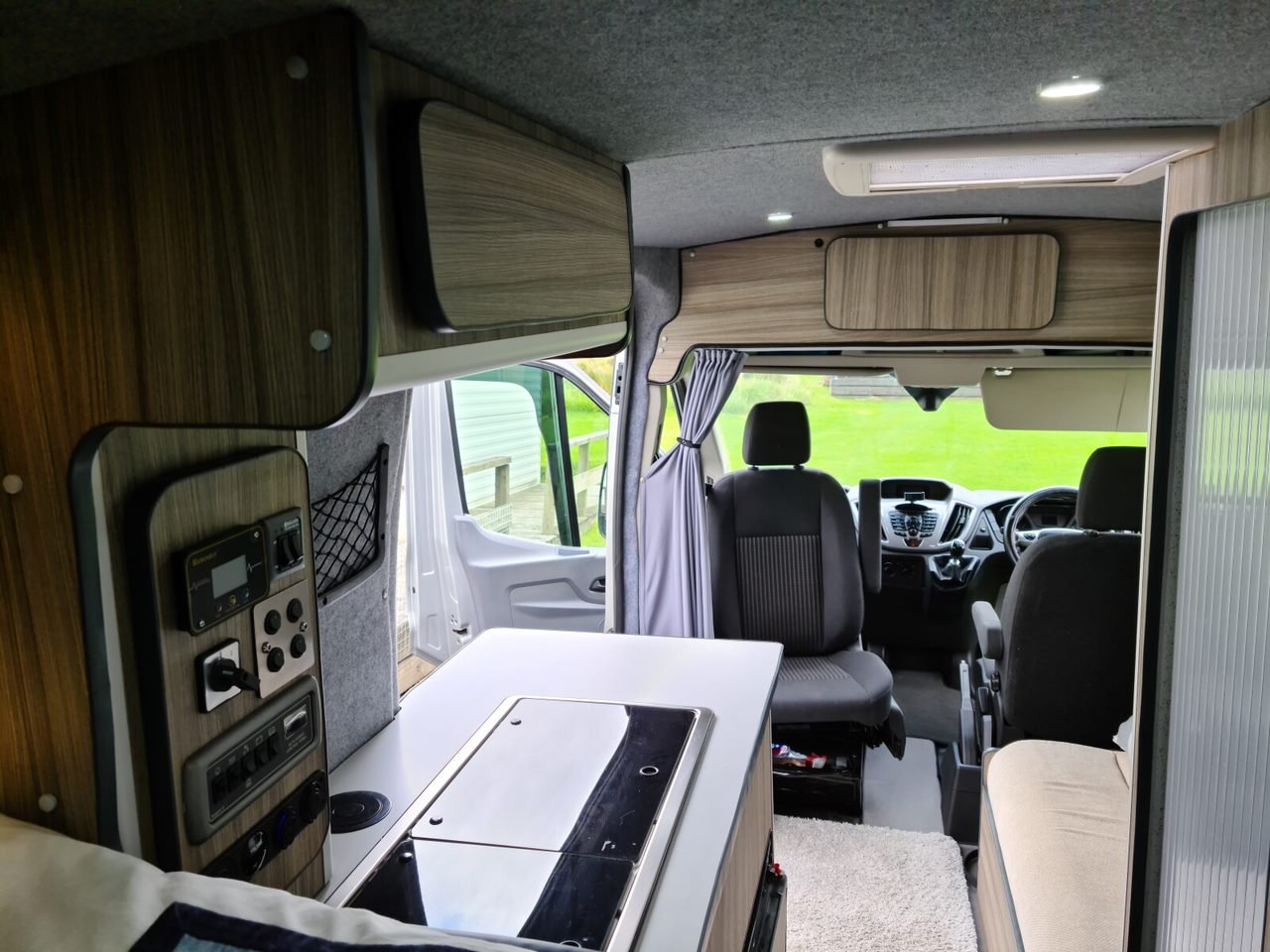 Interior of a small camper van showing the front seats, dashboard, and a compact kitchen area with cabinets and a stove.