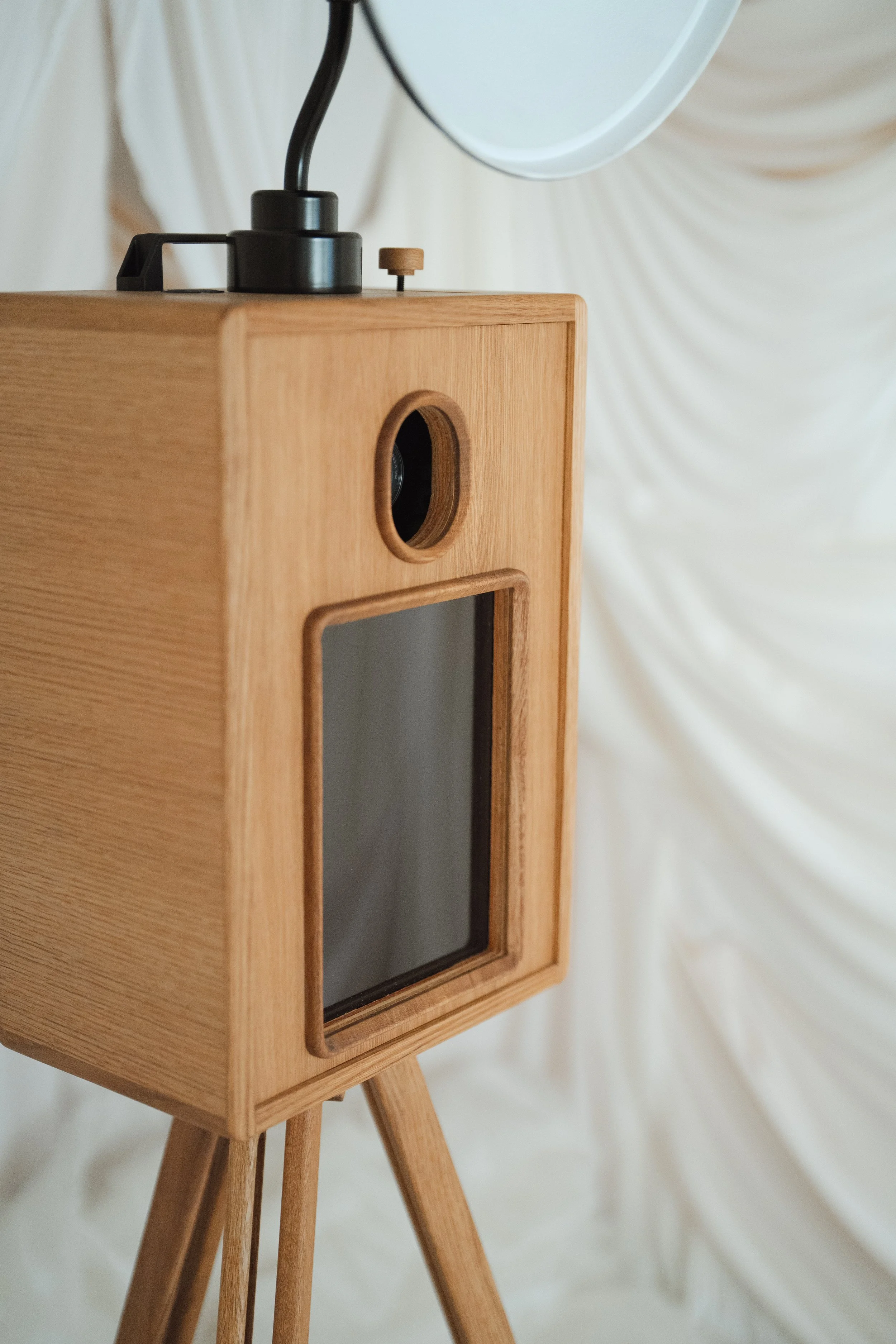 A wooden vintage-style photo booth with a camera lens and viewfinder, standing on wooden legs.