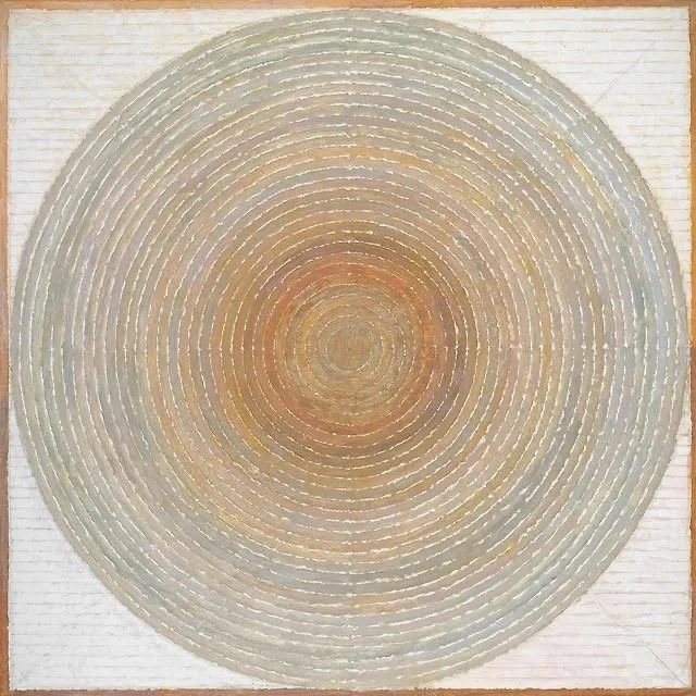 Close-up of a circular, concentric pattern with pastel colors on a textured, light-colored background.