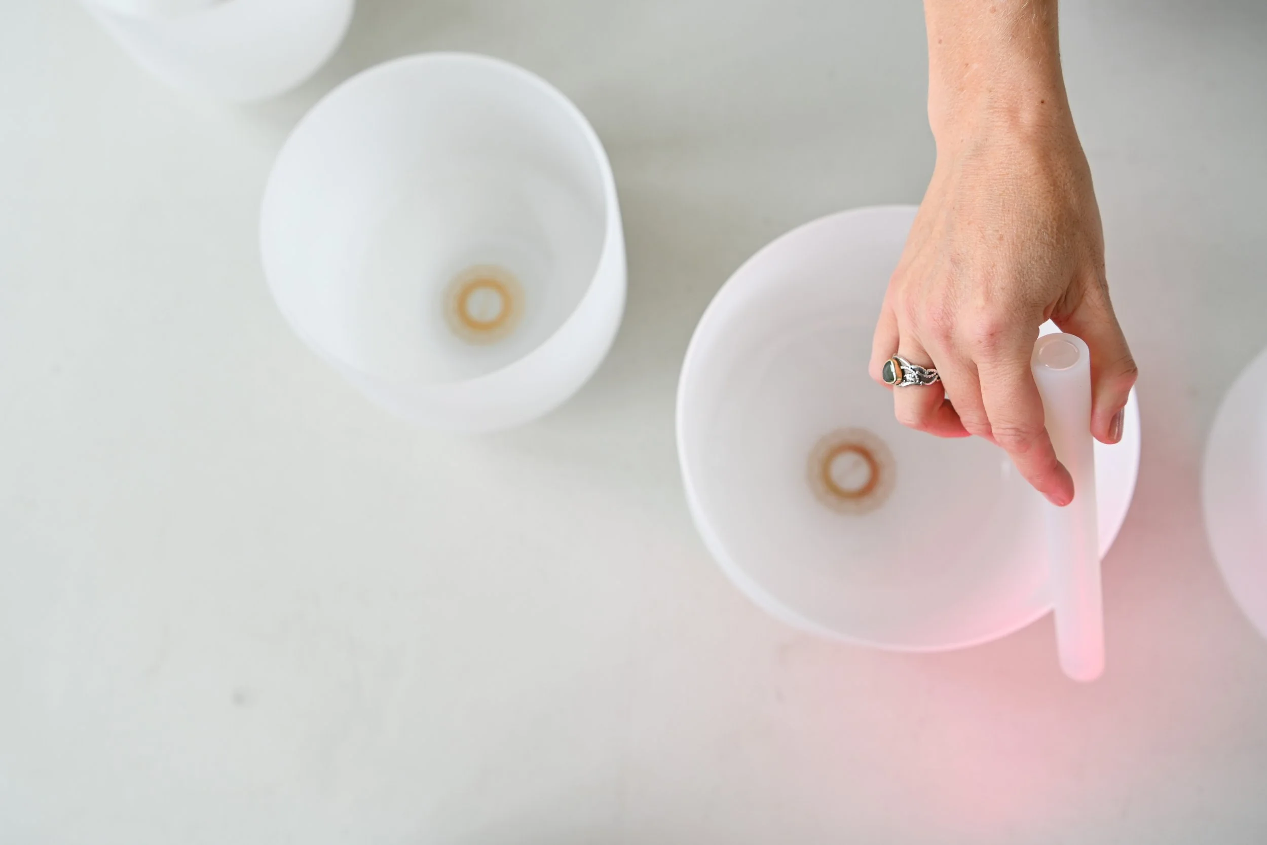 A person's hand holding a small white instrument over a white bowl with a brown stain at the bottom, with two other white bowls nearby on a white surface.