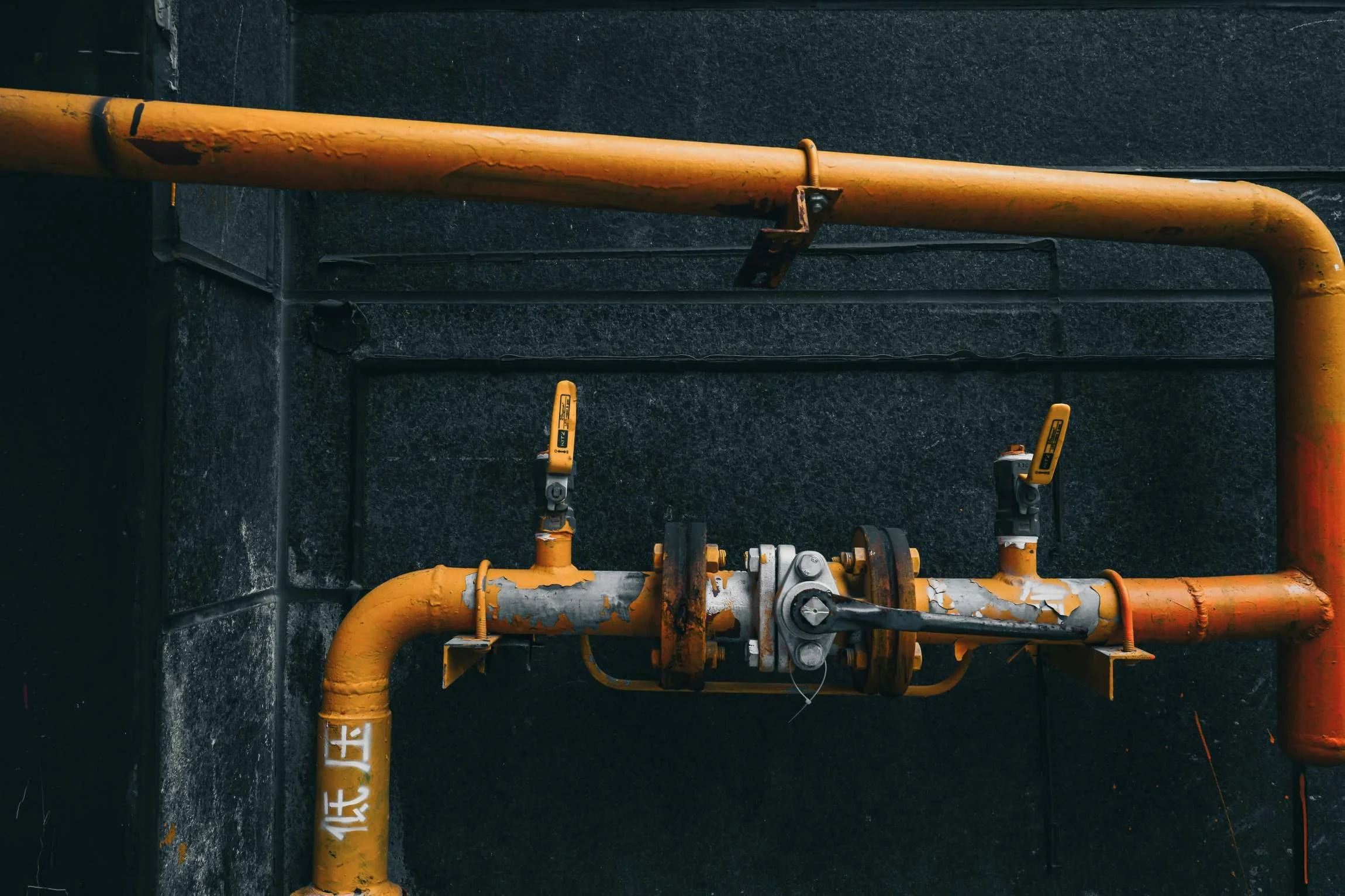 Yellow industrial piping with valves and controllers mounted on a black wall.