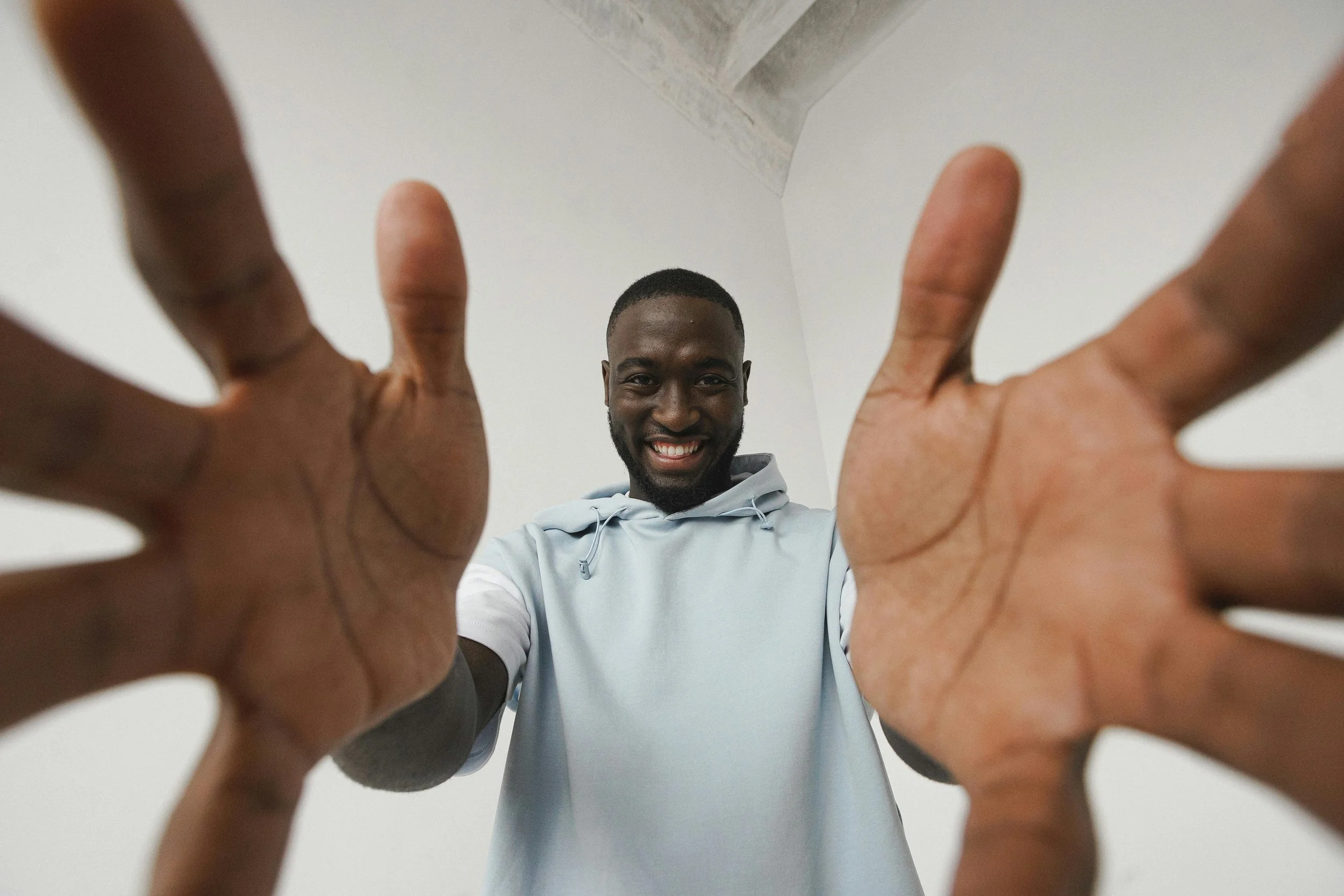 Smiling man in light blue hoodie reaching towards the camera from below.