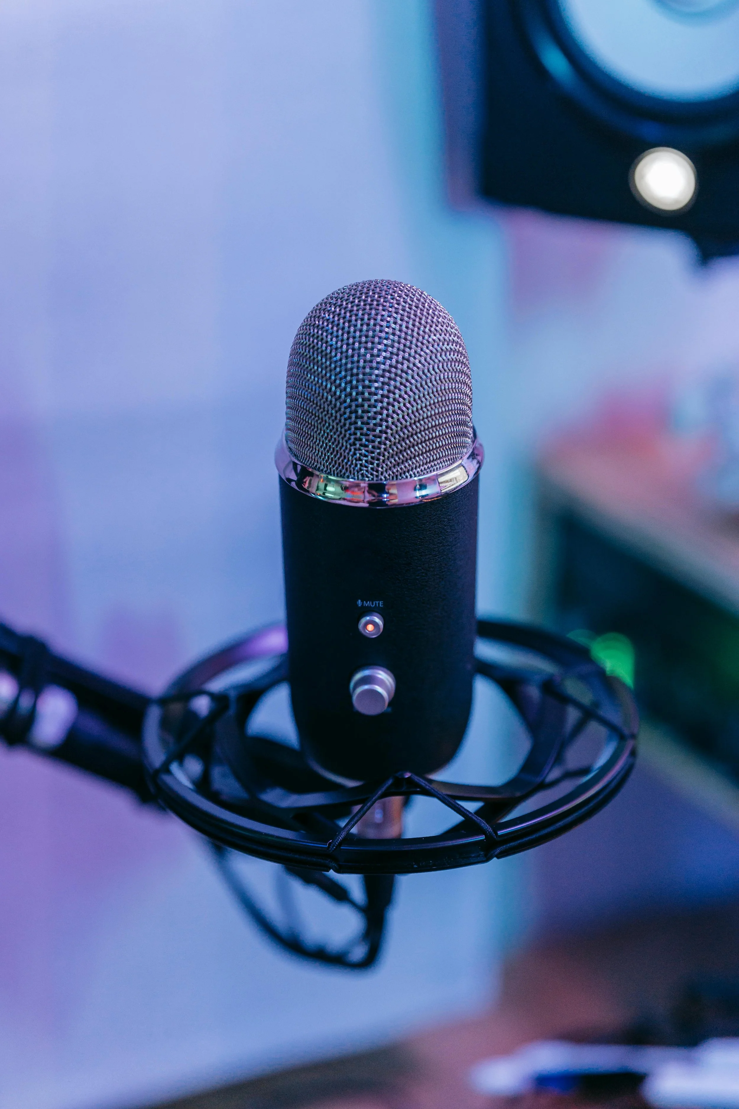 A professional microphone on a stand with a pop filter in a recording studio, illuminated with blue and purple lighting.