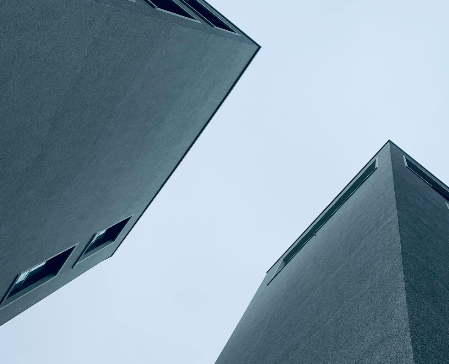 Looking up at two tall, modern apartment buildings with a pale blue sky between them.