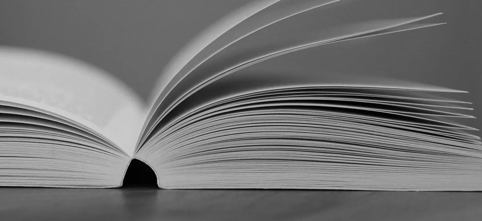 A black and white photograph of an open book with pages fanned out.