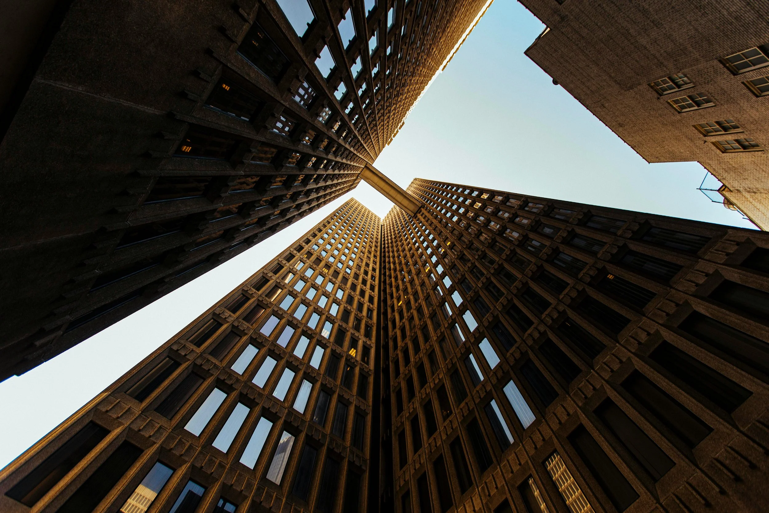 Looking up at tall skyscrapers with glass windows from the ground, forming a rectangular opening to the sky.