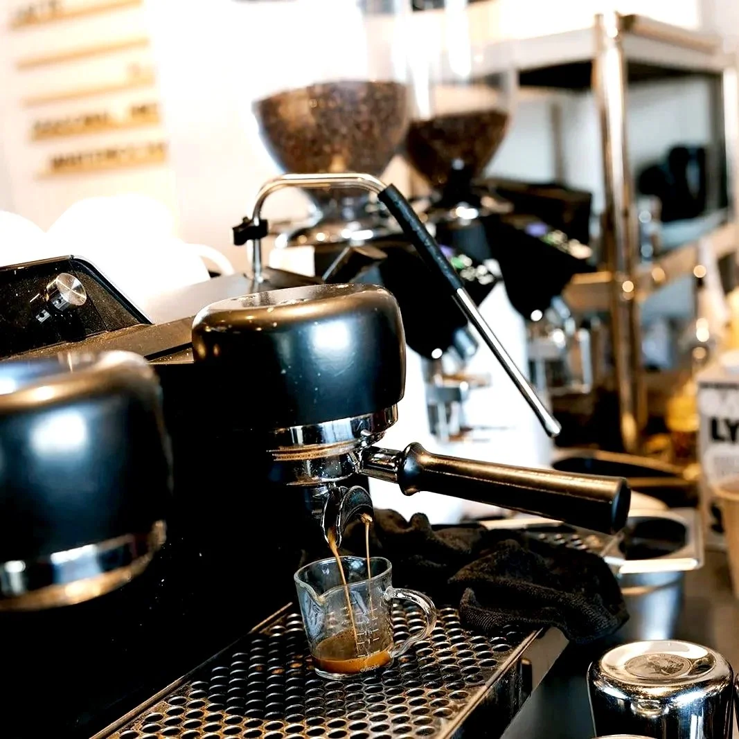 Close-up of a coffee machine brewing espresso into a small glass cup in a coffee shop.
