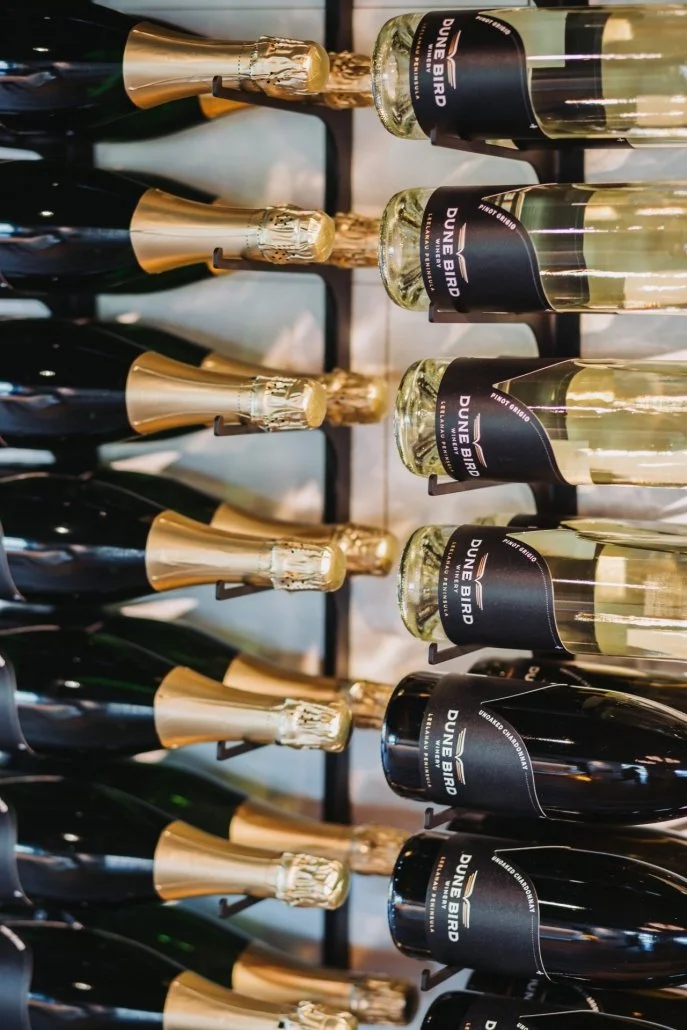 Rows of champagne bottles with black labels and gold foil caps on a wine rack.