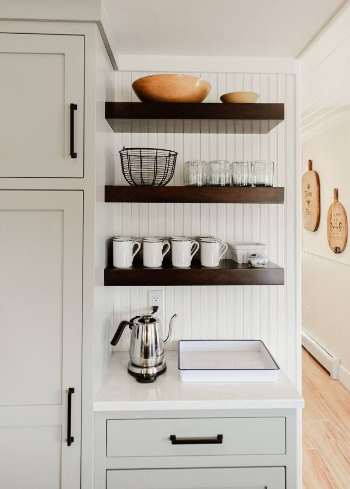 Kitchen shelf with bowls, a wire basket, glasses, white mugs, and a teapot.