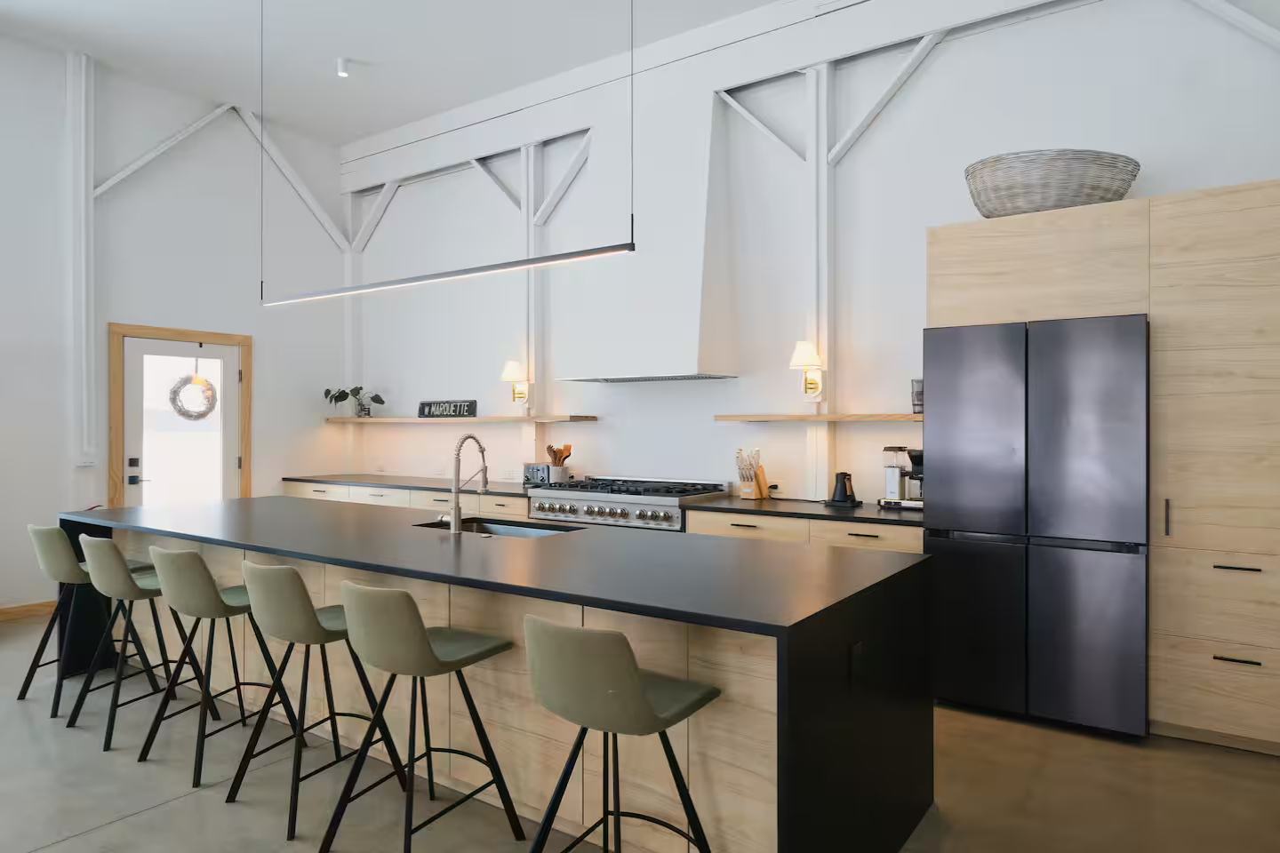 Modern kitchen with black island, beige chairs, white cabinets, black refrigerator, and minimal decor.