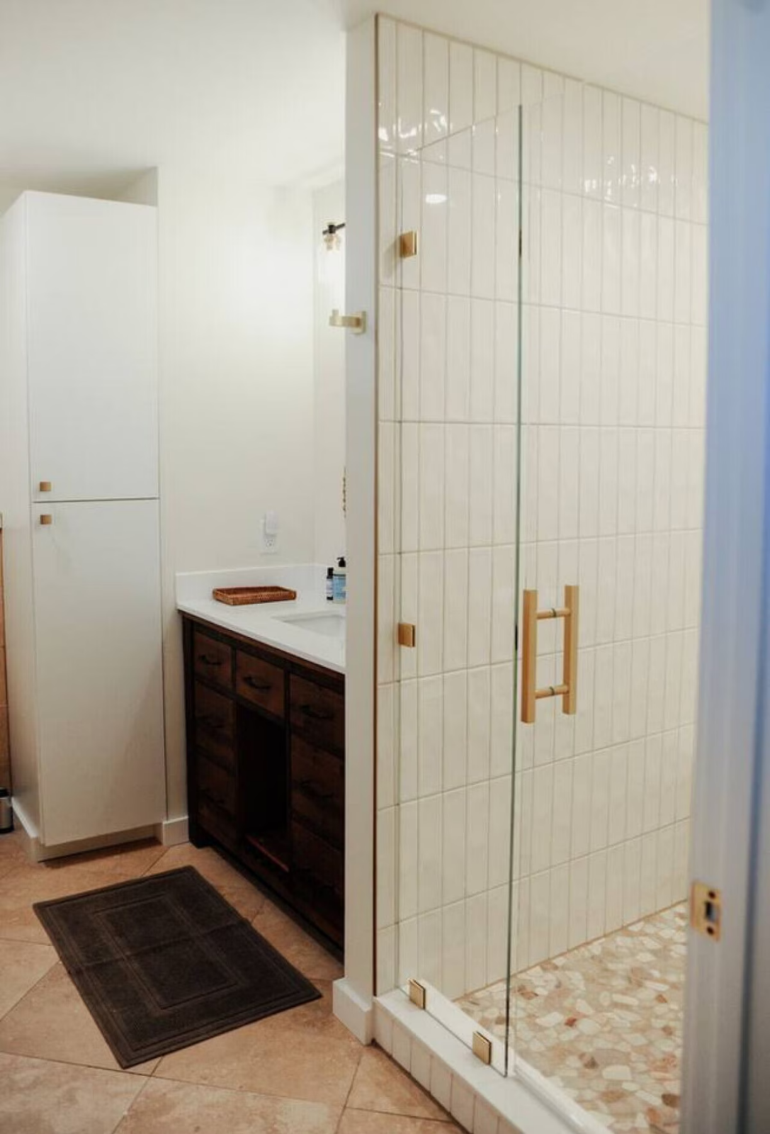 Bathroom with a glass shower door, wooden handle, white tiled walls, and a dark wood vanity with a white countertop and a small sink.