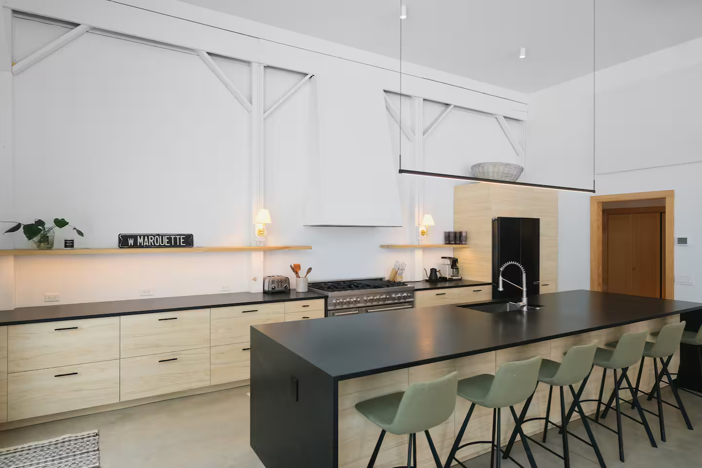 Modern kitchen with black island countertop, beige cabinetry, stainless steel appliances, and light green barstools.