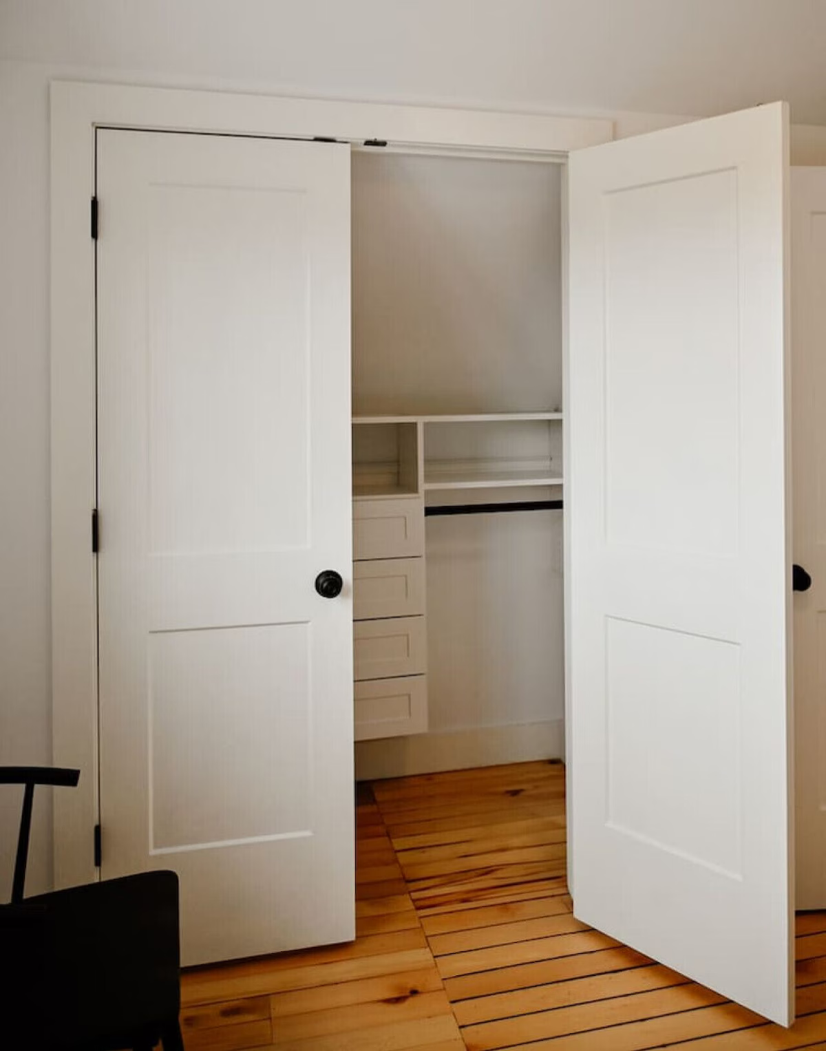 Open white closet doors revealing shelves and drawers inside a room with wooden flooring.