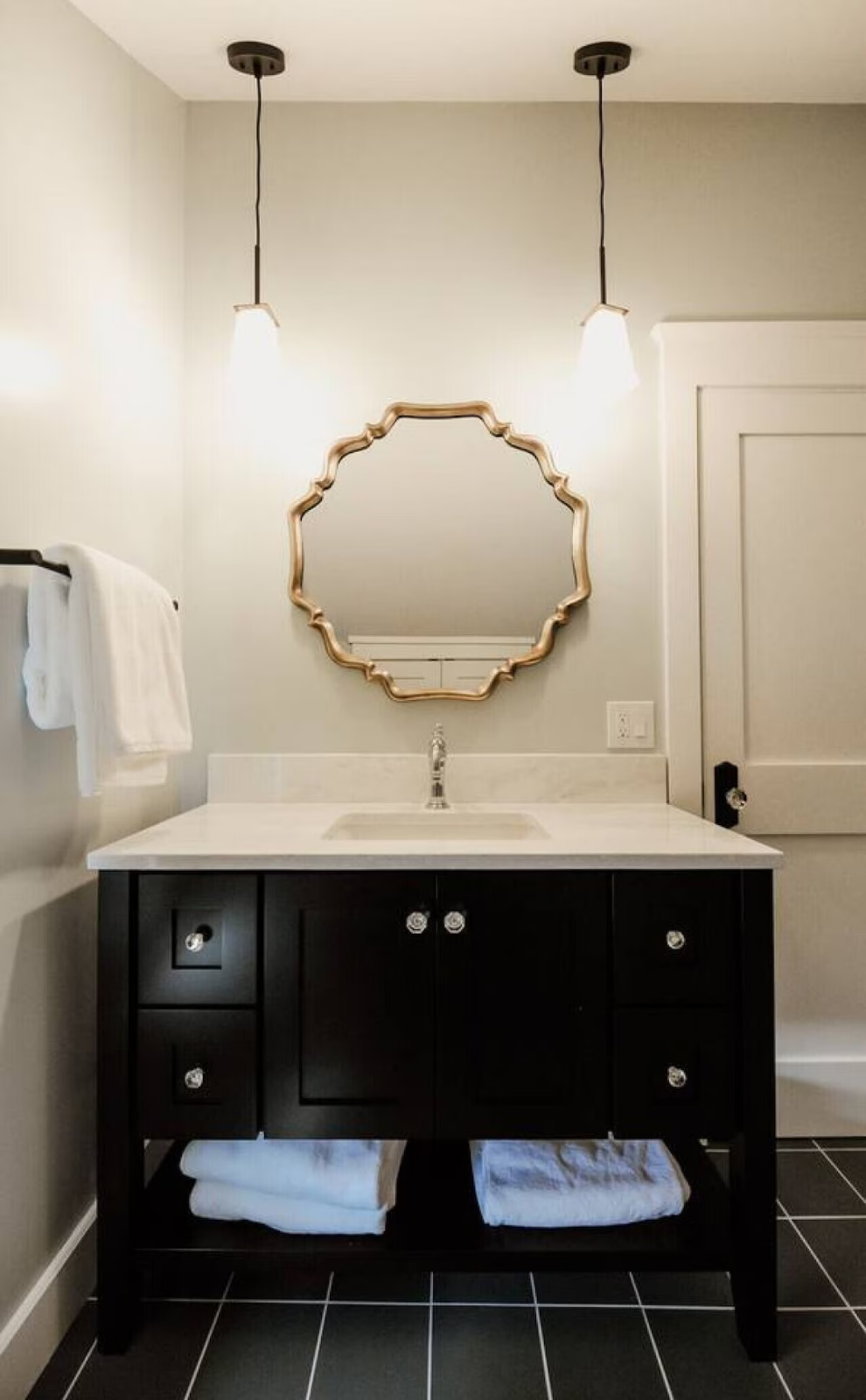 Bathroom with black vanity, white countertop, round mirror, two pendant lights, towels, and tiled floor.