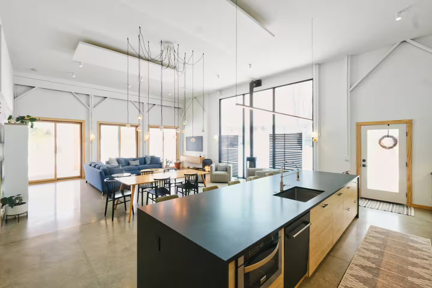 Open-concept living space with a kitchen island, dining area, and seating area with large windows and minimalist decor.