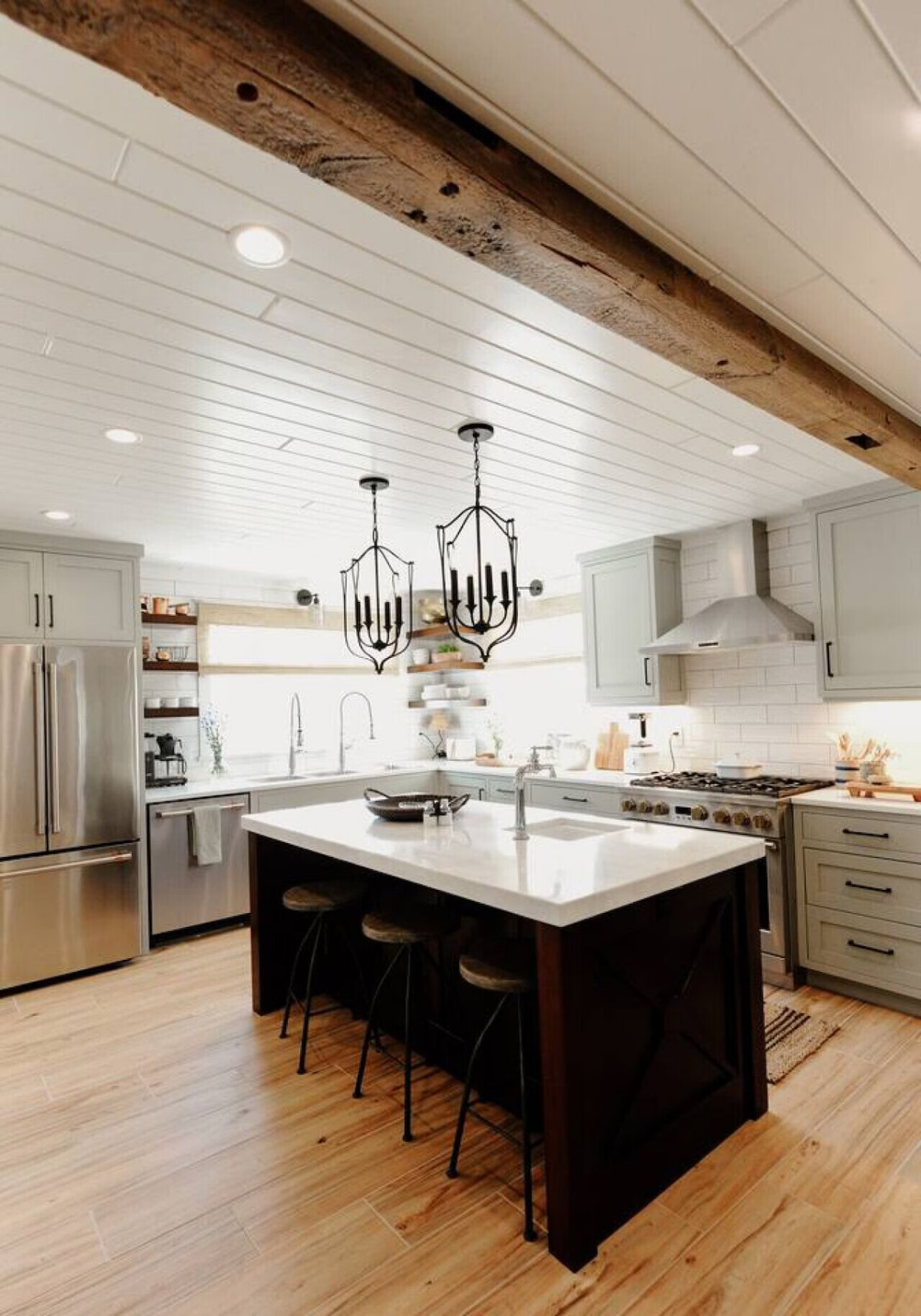 Modern kitchen with light green cabinets, stainless steel appliances, a white island with dark wood sides, and black chandelier pendant lights.