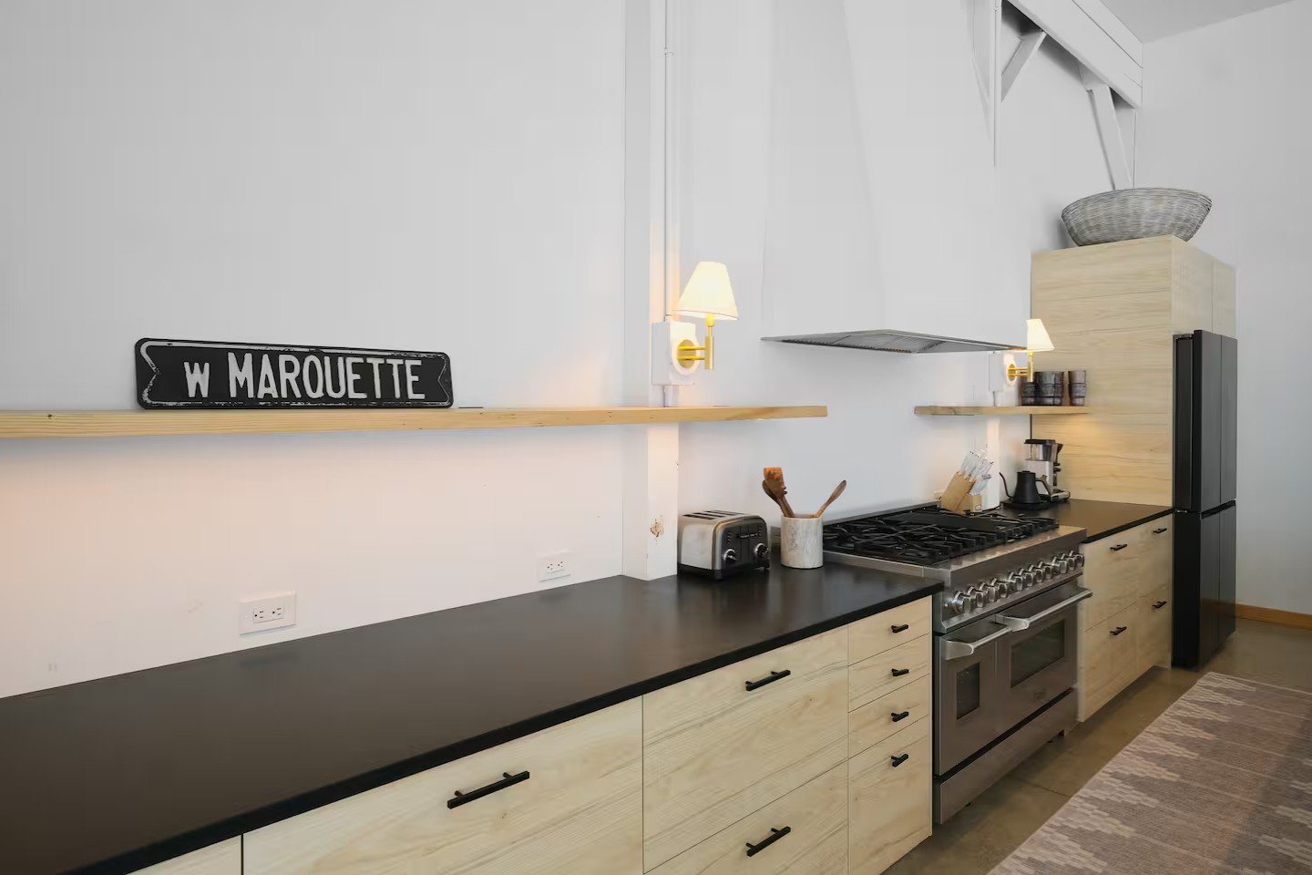 Modern kitchen with black countertops, light wood cabinets, a gas stove, and minimal decor.
