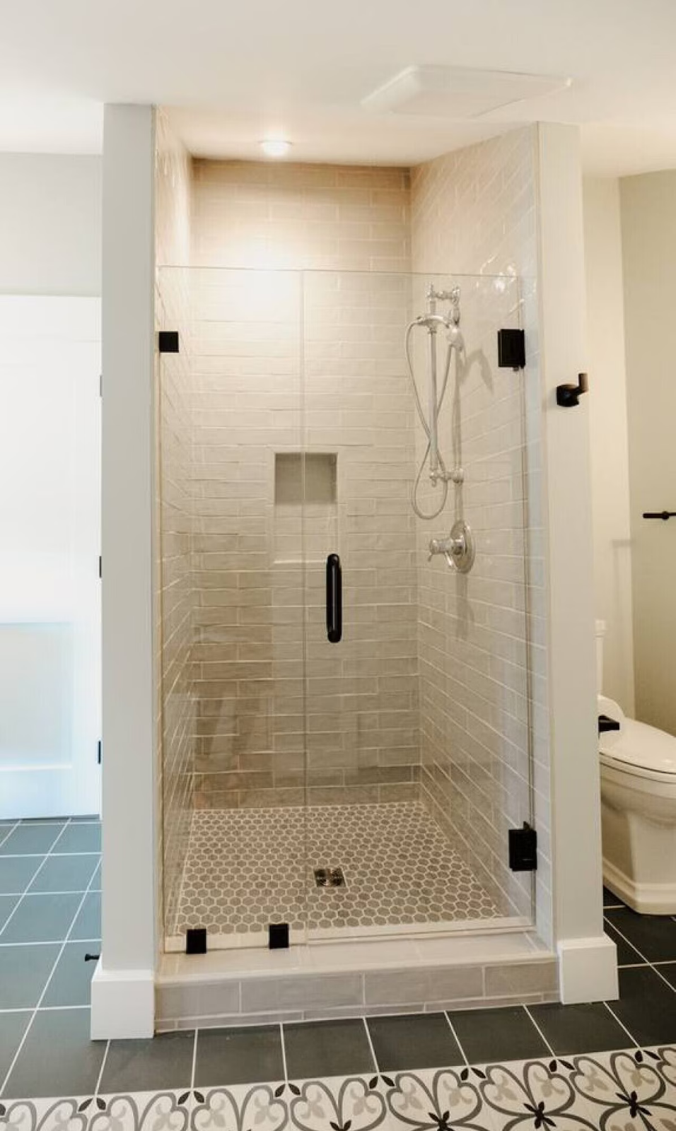 A modern walk-in shower with glass enclosure, beige brick-like tiles, a built-in niche, and a handheld showerhead in a contemporary bathroom.