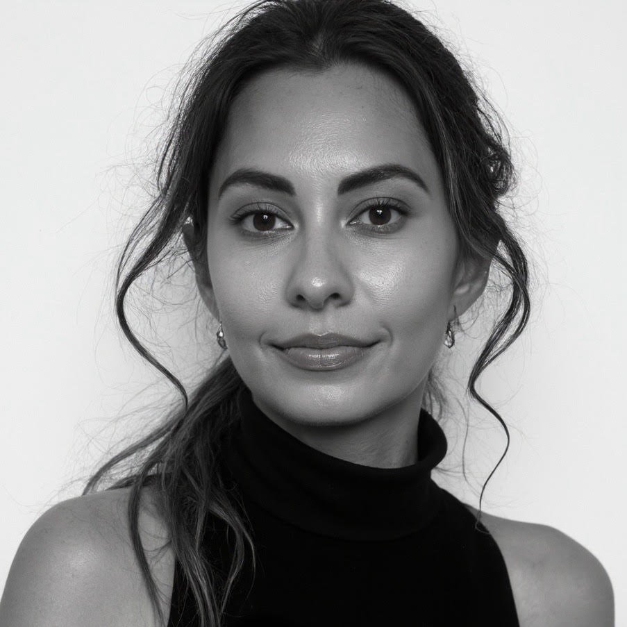 Black and white portrait of a woman with wavy hair, wearing a turtleneck and earrings, looking directly at the camera with a slight smile.