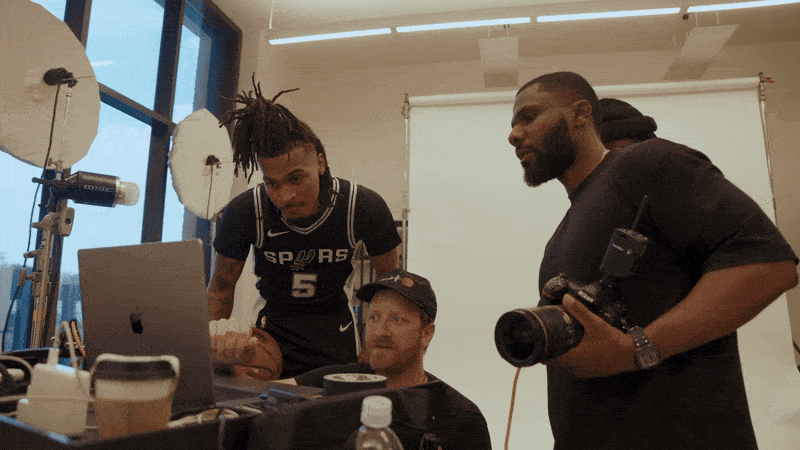 Three men working on a photo or video shoot indoors, with a laptop and camera equipment on the table.