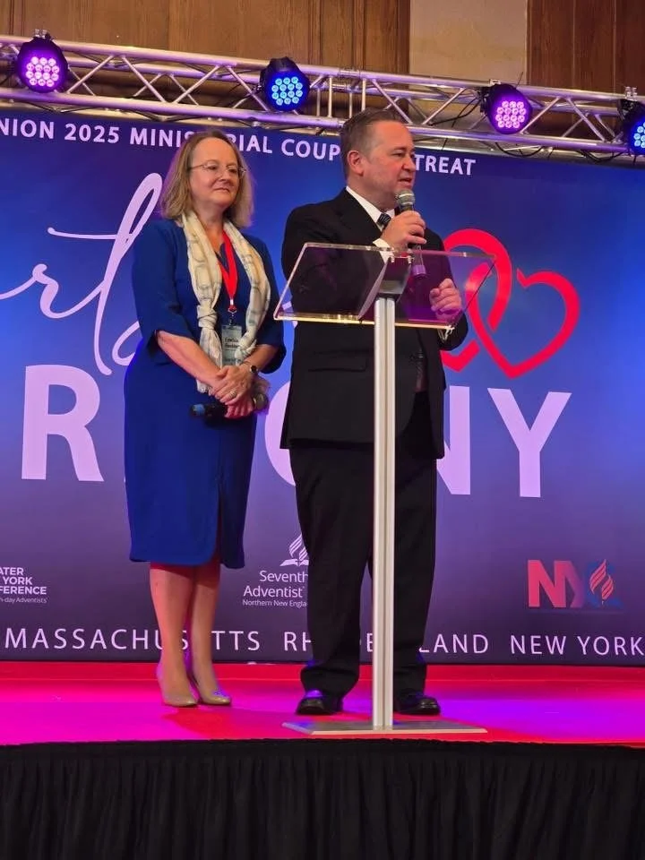 A pastor and his wife stand in front of a large banner leading a marriage seminar for a church conference.