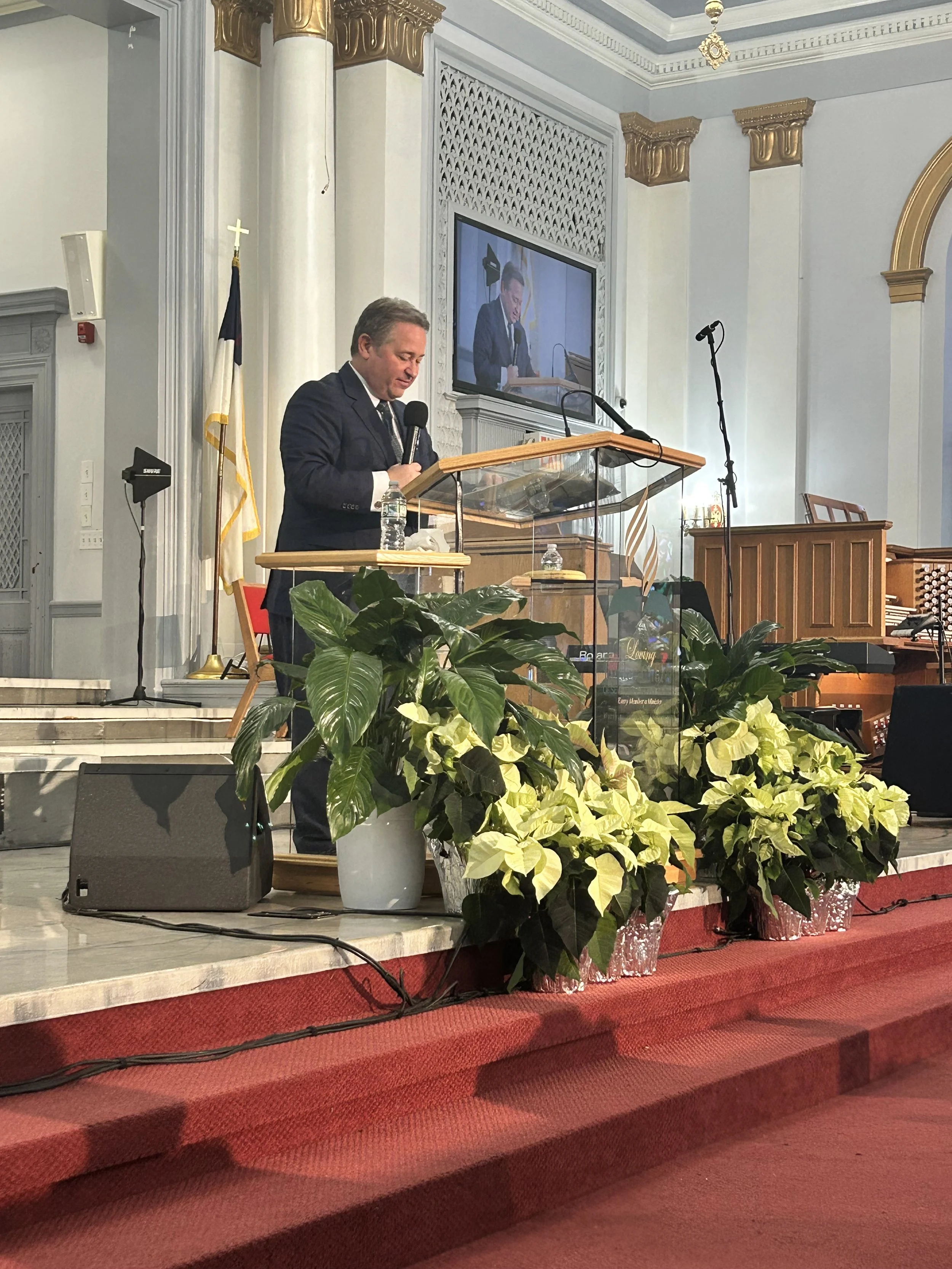 A pastor stands at the altar in a nice modern church leading prayer. Board and Leadership Development.